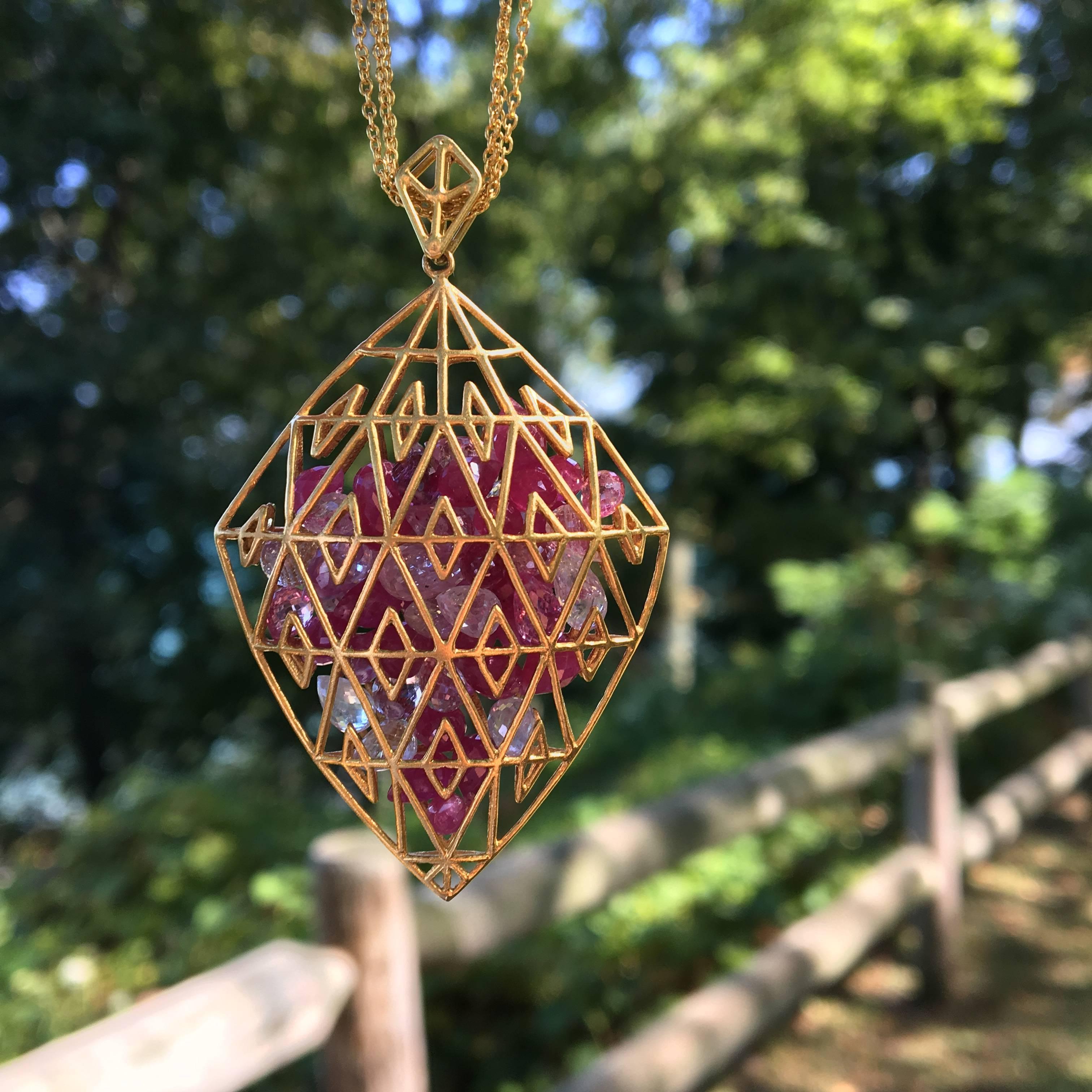 This pink sapphire and 18kt Gold pendant is a creative and playful work of art.  Shades of dark to light pink loose sapphires are loose and free to move around securely inside the 18kt matte gold cage pendant.  

30 inches of 3 separate 18kt Gold