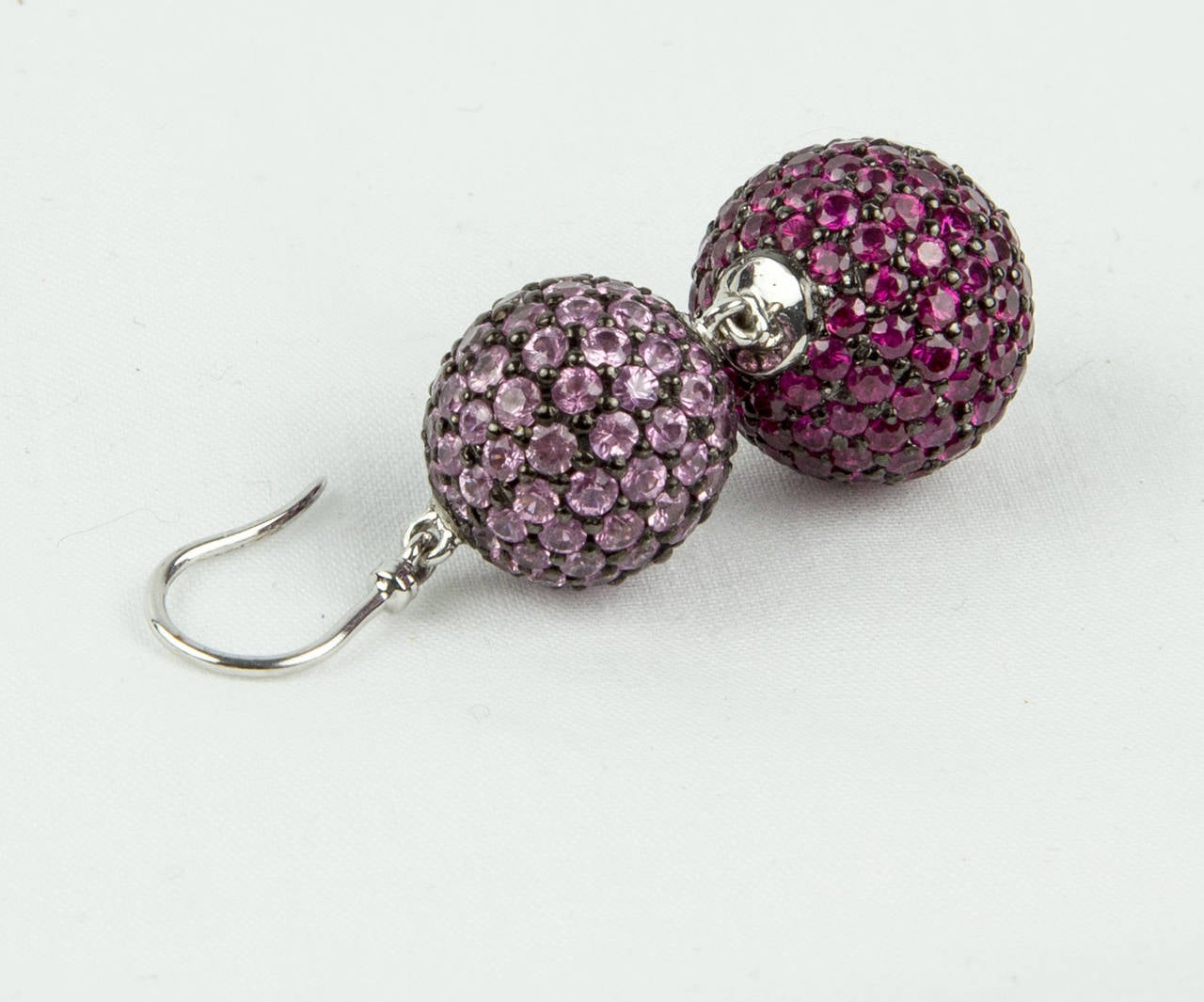 Striking pair of Dangle Drop Earrings, featuring a smaller pavé Pink Sapphire ball, suspending a larger pavé Ruby ball, mounted in 18k white gold; 124 Pink Sapphires weighing approx. 4.96 total carats and 156 Rubies weighing approx. 6.24 total