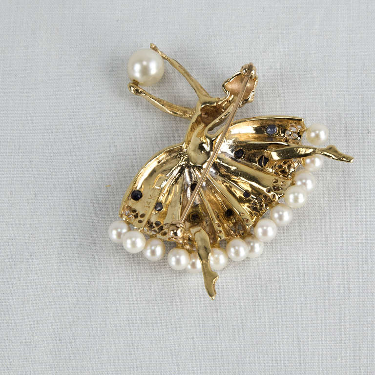 A Leaping Ballerina brooch pin crafted in 14k yellow gold and set with Pearls, Diamonds and Sapphires. Marked: 14K. Approximate size: 2” x 1.75”.