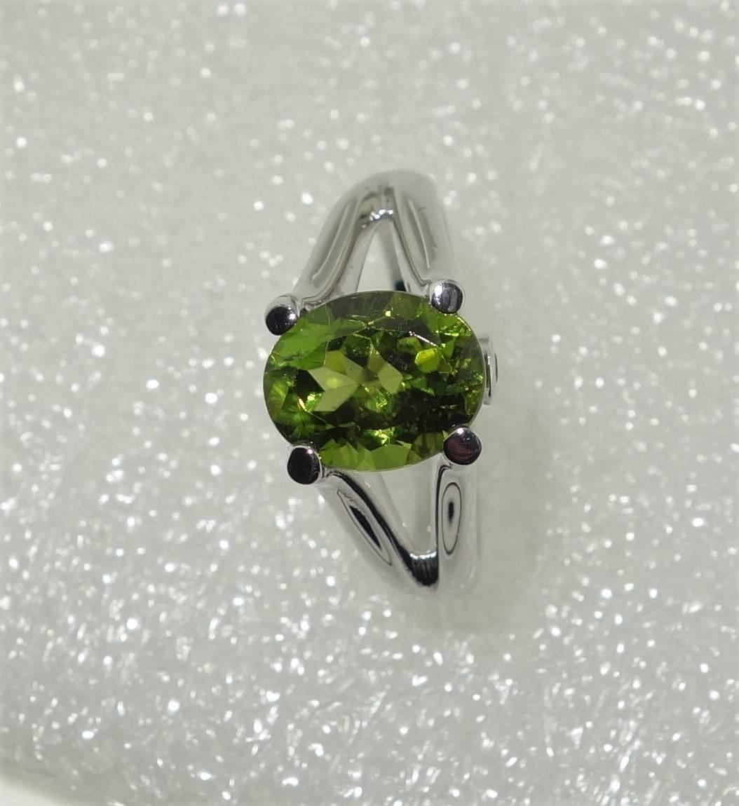Beautiful ring featuring a 3.01ct Peridot, enhanced either side with Sapphires; approx. .08tctw; Sterling Silver Rhodium Tarnish-resistant mounting. Size 7; Classic and Classy …illuminating your look with Timeless Beauty!   
