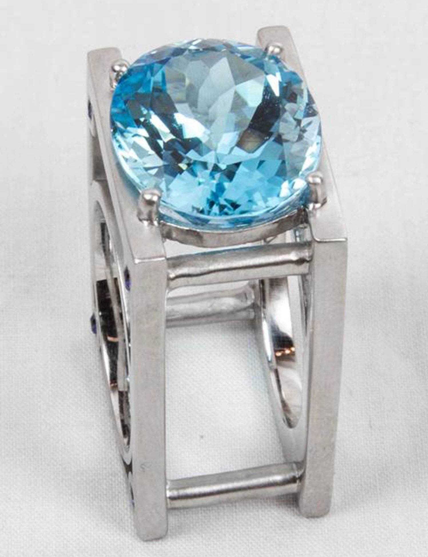 Sensational Sky Blue Topaz Statement Ring set with a large oval 23.62ct facet-cut blue topaz and 8 'rivets' set with small blue sapphires; .36ct; in a unique Industrial style Sterling Silver Rhodium Tarnish-resistant Satin finish mounting. More