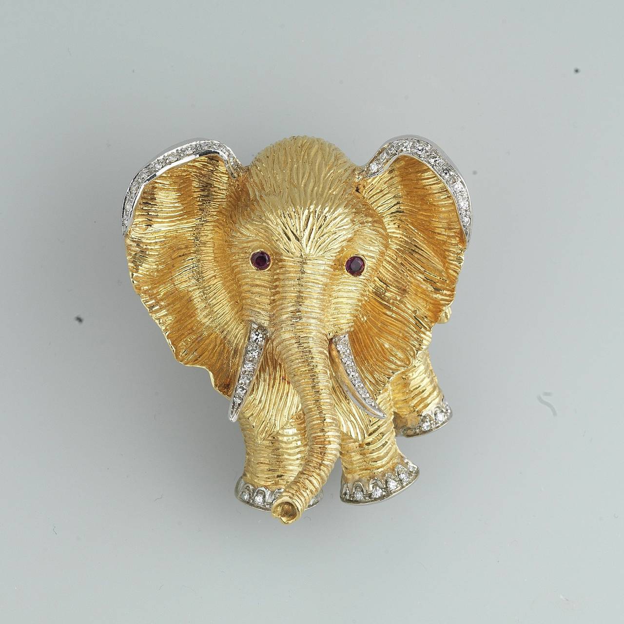 A gold, ruby and diamond Elephant brooch.
Sculpted gold elephant brooch, set on platinum with circular-cut diamond detail and ruby eyes.
Italian marks for gold 18Kt. Circa 1960.

Height: 1.97 in. (5.00 cm.)
Width: 1.58 in. (4.5 cm.)
Thickness: