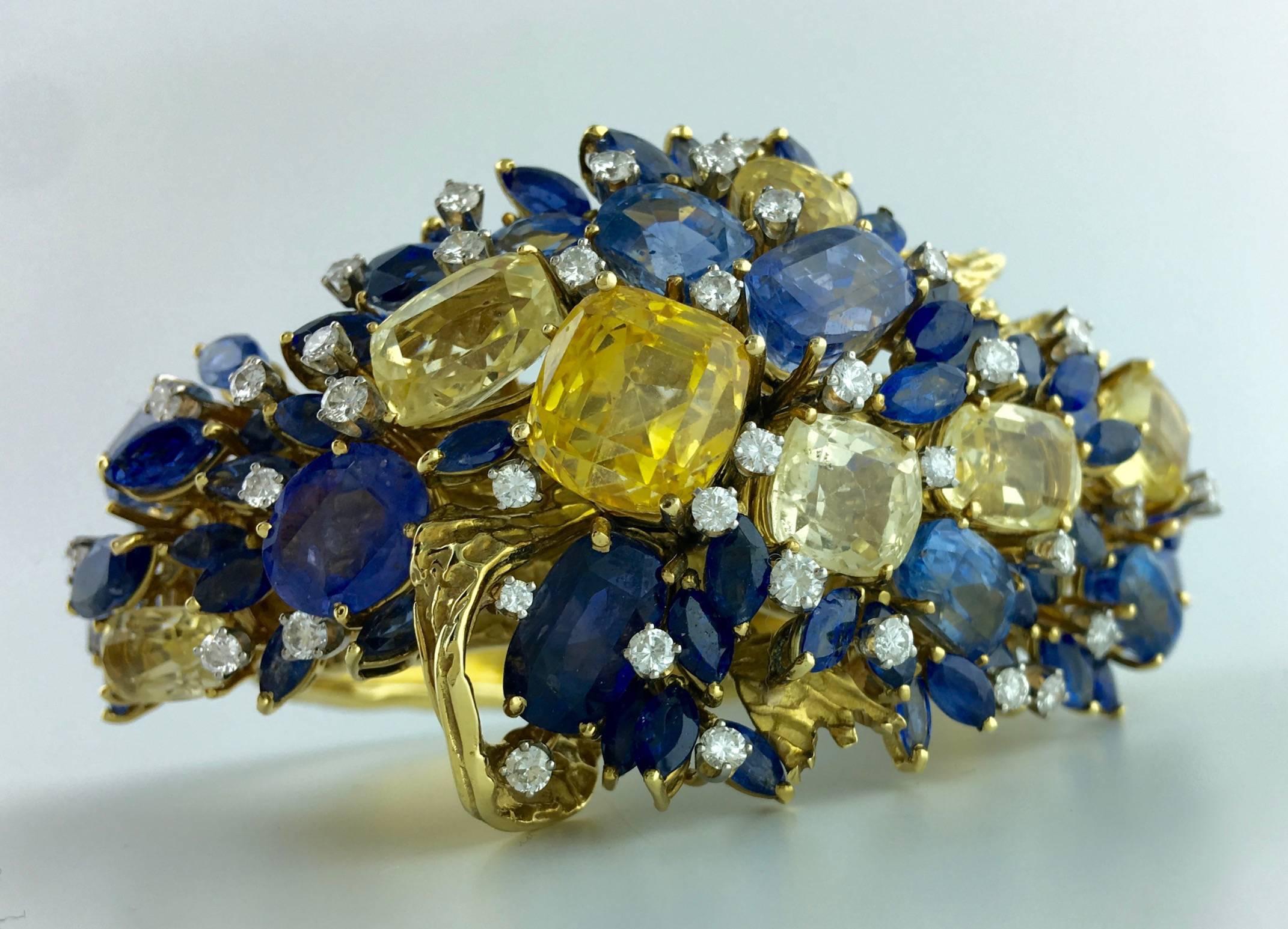 Unbelievable!
Designed as a floral cluster of cushion, oval and marquise-shaped sapphires of various blue and yellow hues, accented by round diamonds, on a textured gold 18k hinged bangle. 
American jewel reminding the work of jewellers as
