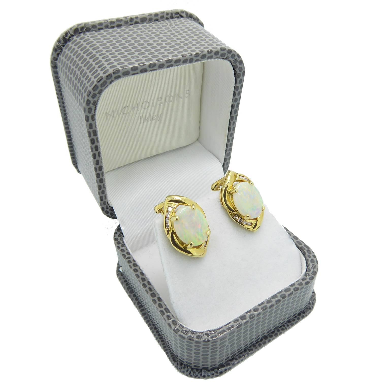 Oval cabochon cut opals in yellow claw settings within an irregular oval gold surround and embellished with a curved row of brilliant cut diamonds.  The earrings are on gold posts for pierced ears and fasten with a sprung gold clip.