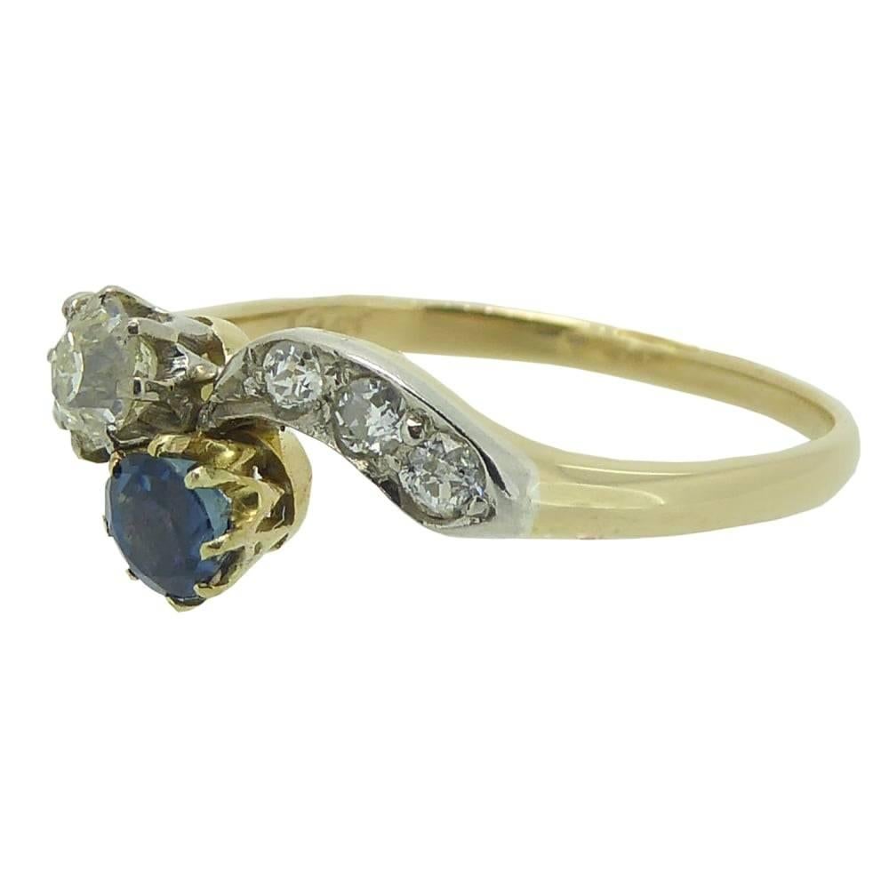 Pretty and elegant vintage engagement ring set the a round, mixed cut sapphire of rich blue colour and a round brilliant cut diamond in a cross over design.  The gemstone have both been mounted in yellow rex settings to curved, white metal topped