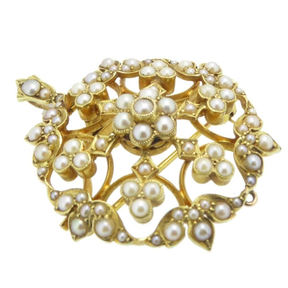 An Edwardian seed pearl set pendant/brooch consisting of a circular, open-work foliate design panel measuring 30mm diameter and grain set with split seed pearls measuring 1.2mm -2.4mm diameter, assessed as natural.  The pendant/brooch suspends from