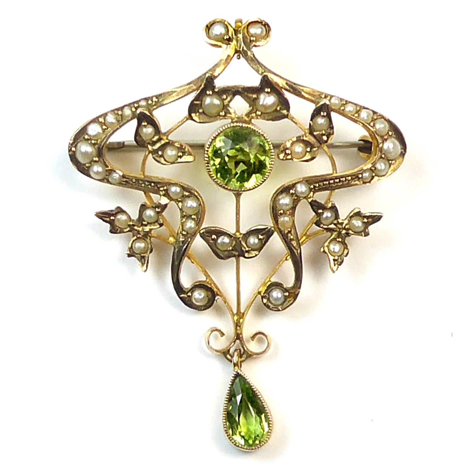 An exquisitely proportioned Art Nouvea pendant centring on a round millegrain set peridot of rich green colour.  The peridot is surrounded by a swirling gold wire-work frame encrusted with pearls, the frame being puncutated by pearl set leaves and