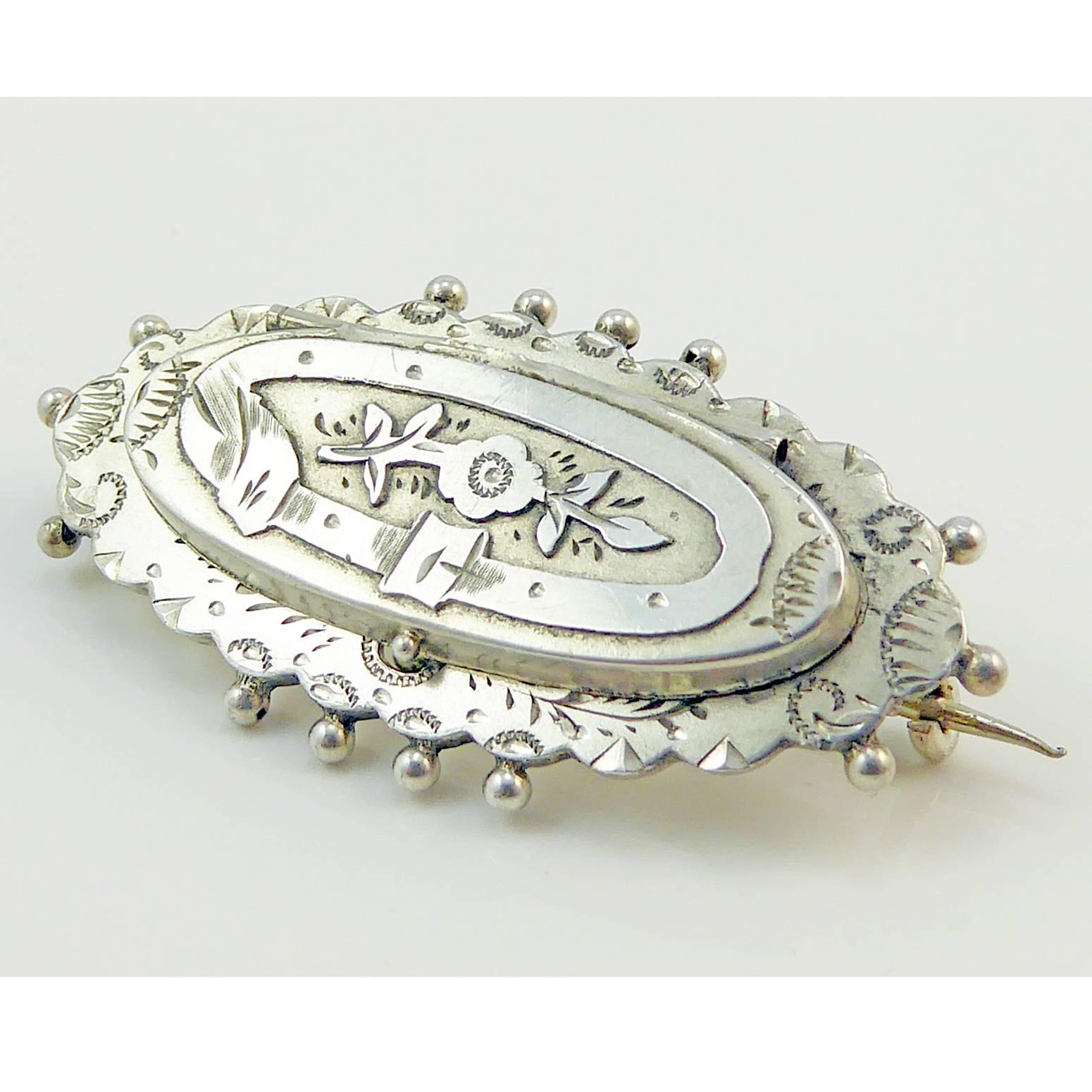 A beautiful antique silver brooch with a hidden message.  In an oval shape with scalloped and beaded edge, the brooch has a raised and hinged section with is engraved with the sentimental belt and buckle motif enclosing a forget-me-not flower.  Lift