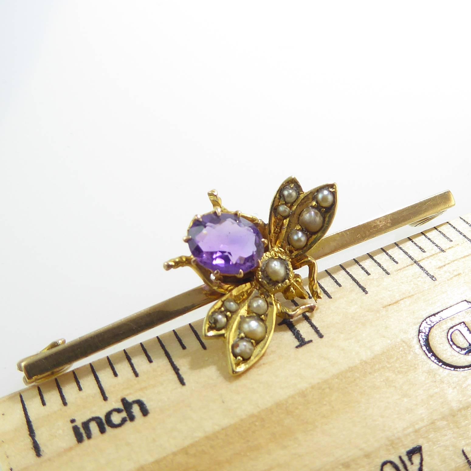 A delightful little bee with an amethyst body and pearl encrusted wings sits at an angle on a gold bar brooch. 

The amethyst is an oval mixed cut held within 10 yellow gold claws to an ope coronet style setting.  A single pearl in a milled grain