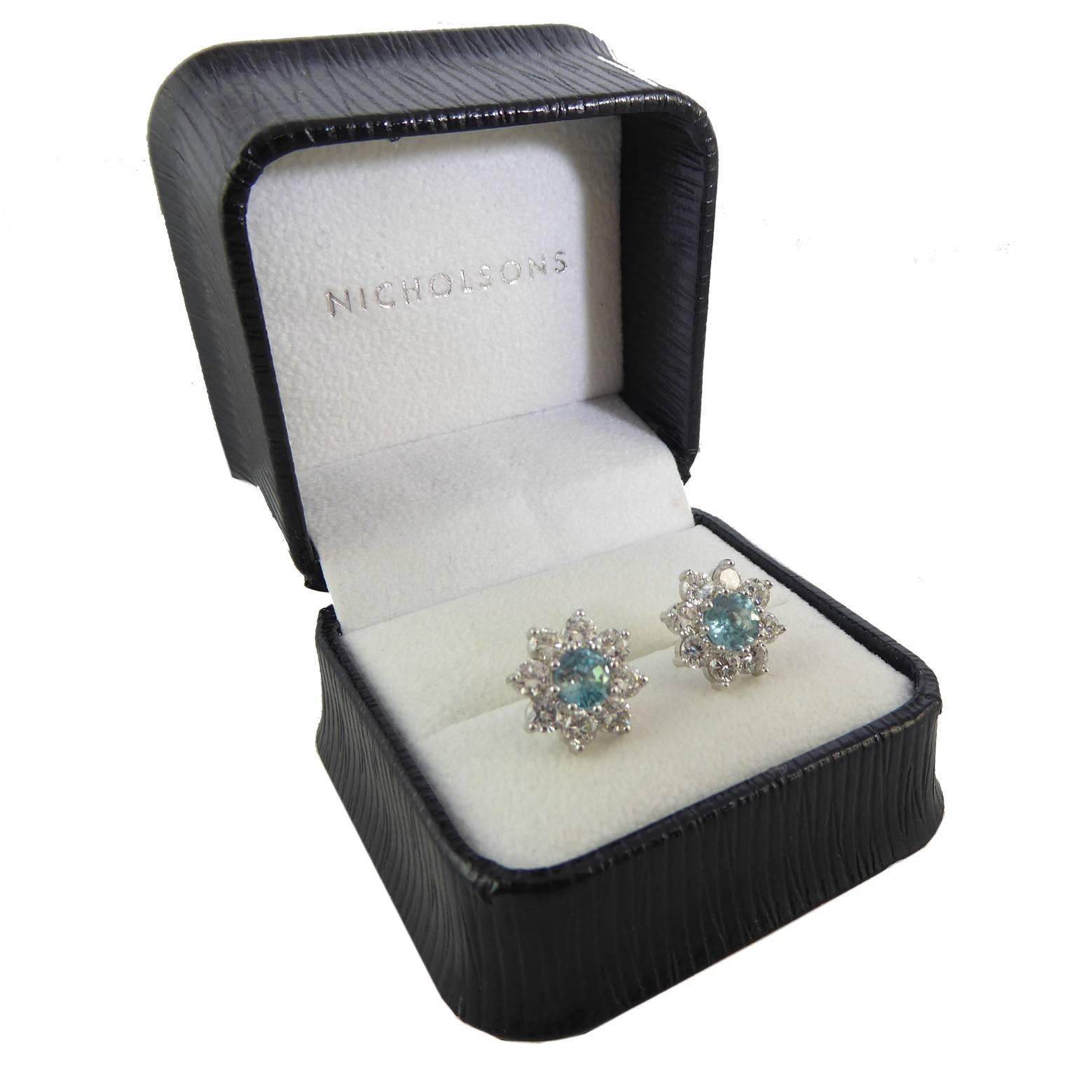 These lovely vintage earrings from the late 20th century have been created in a cluster style.  Each earring is set with a pale greenish blue zircon in a surround of eight round brilliant cut diamonds all claw set in 18ct white gold.  For pierced