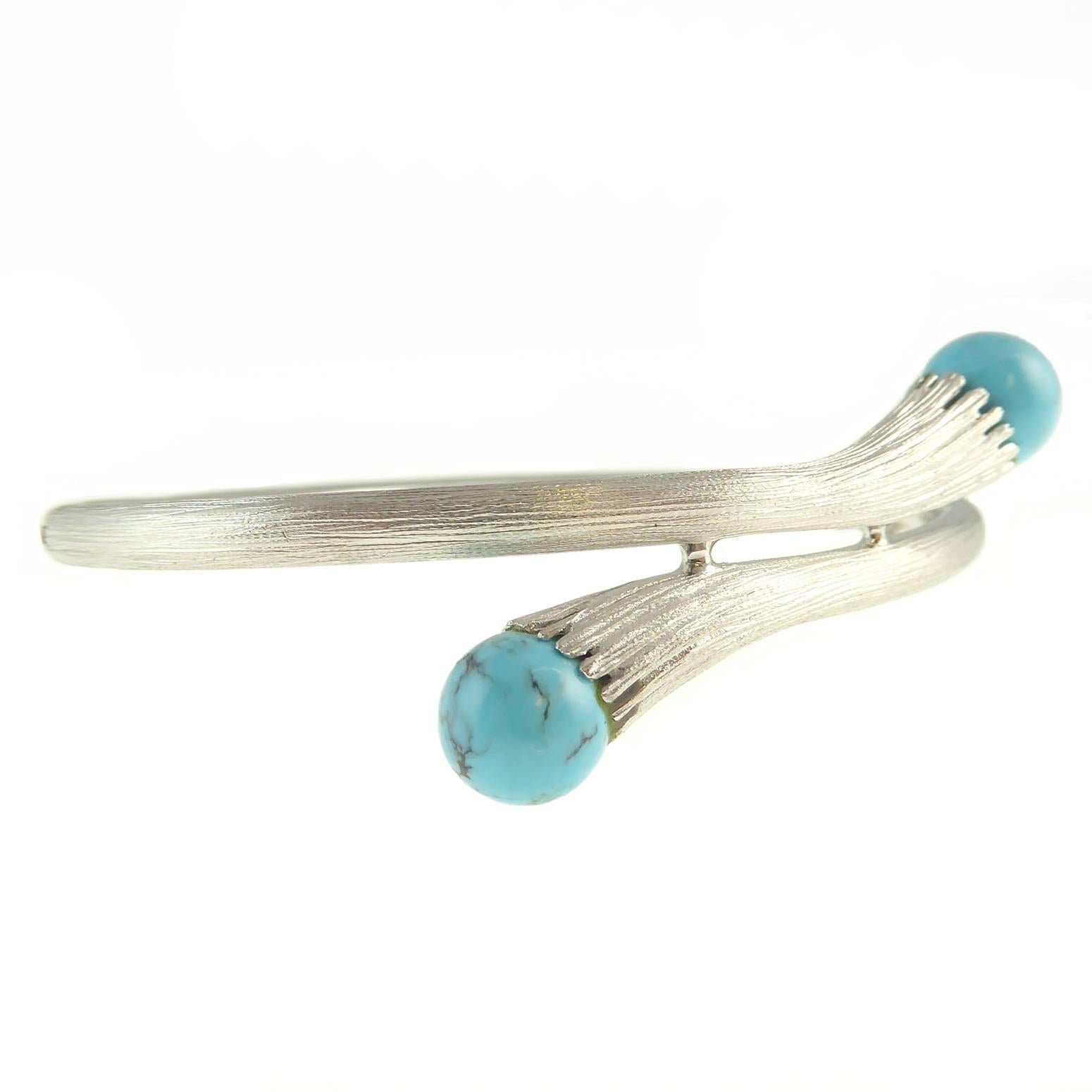 A retro white gold bangle in a pleasing form with a gently swirling cross-over design terminating in a round turquoise of good colour and interesting veining.  

The bangle is hollow, as was quite usual with this type of wrist wear, and displays a