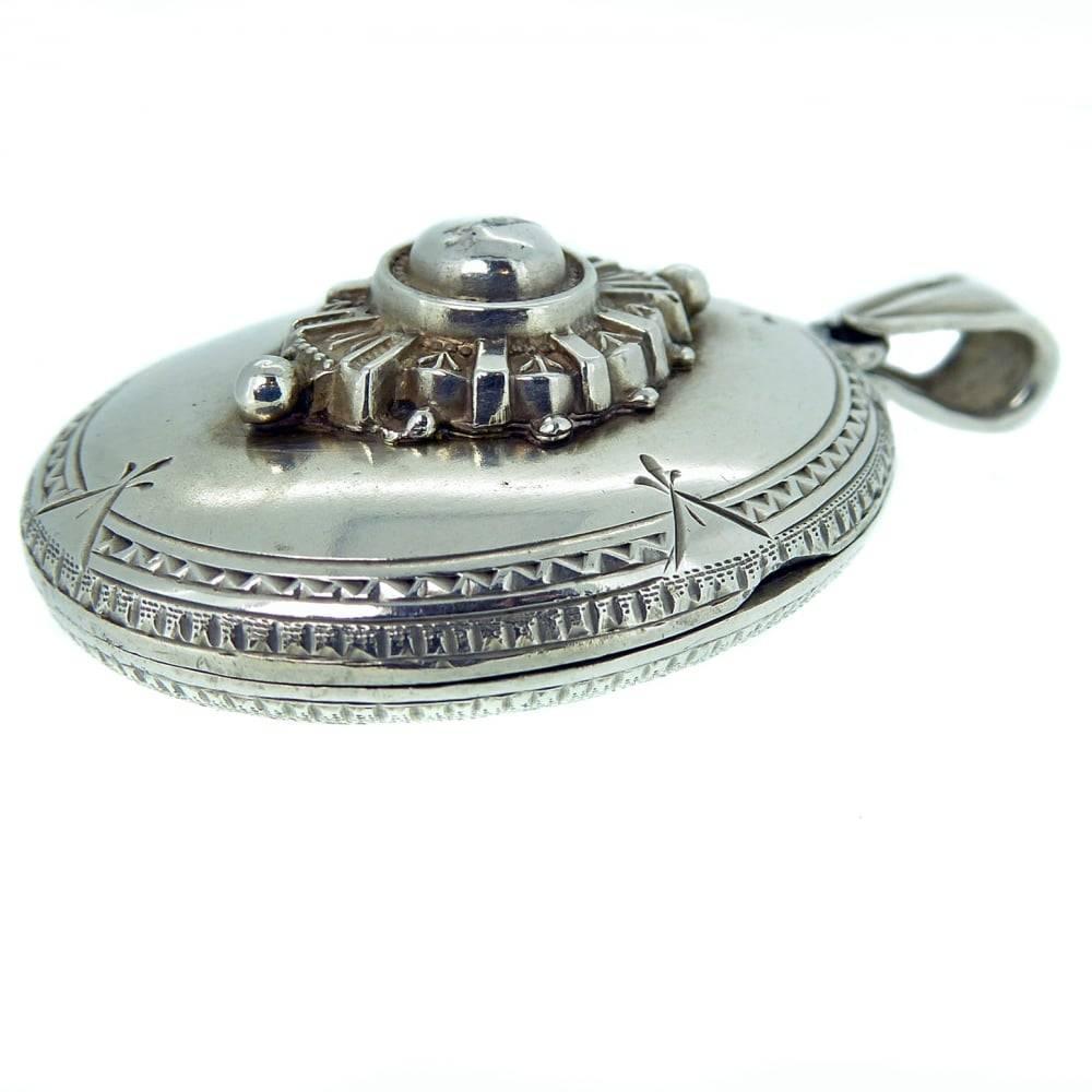 A very ornate silver locket with a delicately engraved edge to the front half and a typically Victorian raised motif to the centre of a central dome surrounded by a sunray and bead edge.  The reverse of the locket also boats some very pretty