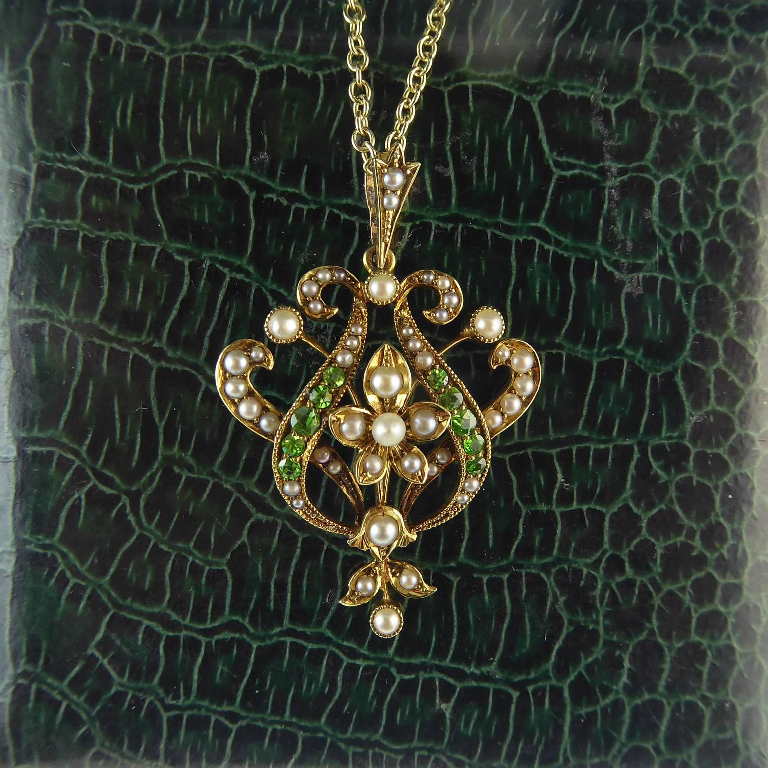 An antique pendant in a very graceful Art Nouveau style design of open wirework around a central pearl set floral motif.  The flower is bordered on either side by a swirl of sparkling demantoid garnets with pearl set curling finials.  Further swirls