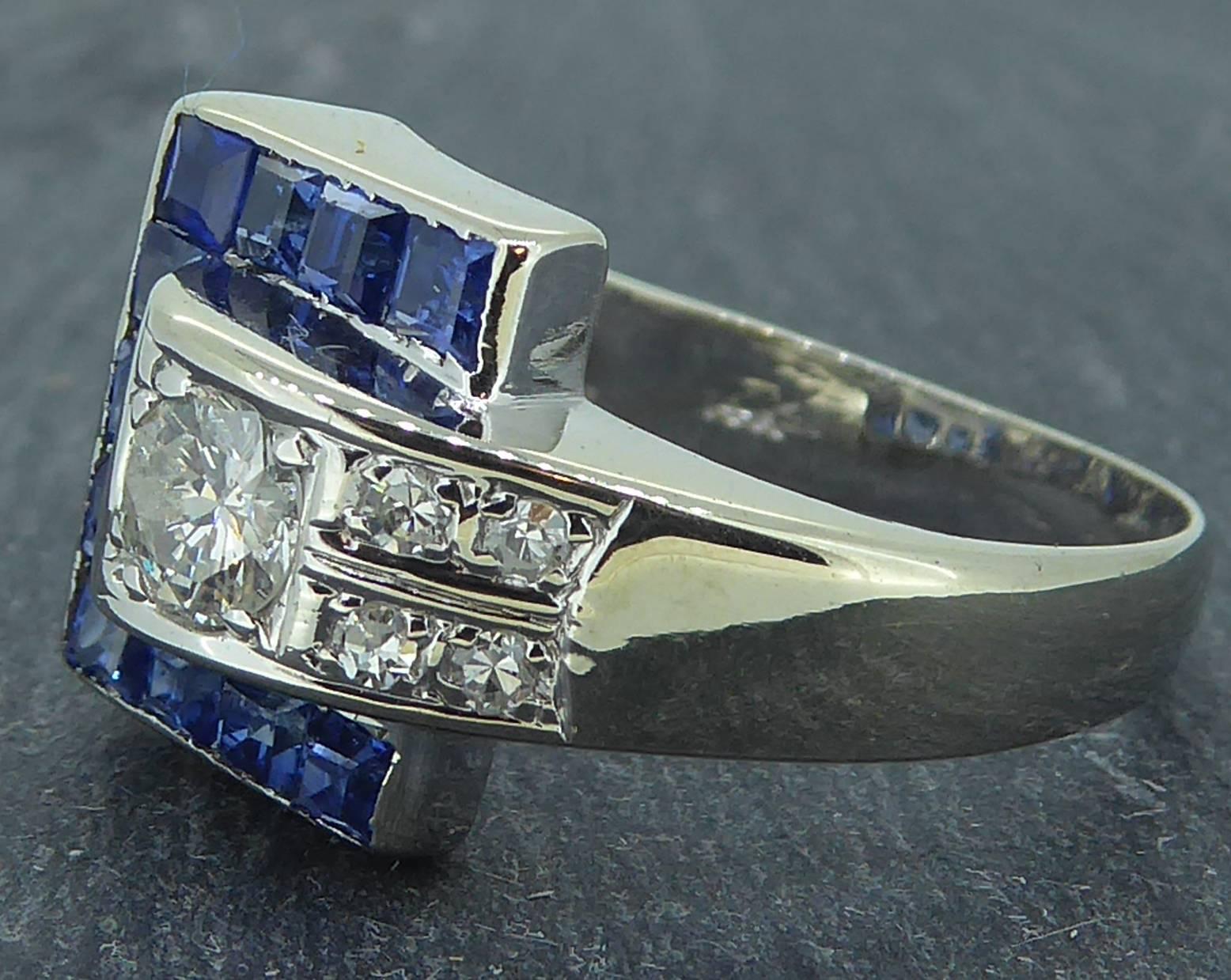 Vintage sapphire and diamond cluster ring from the 1930s/1940s in a buckle style.  A central section of overal square shape and set with step cut sapphire.  A diamond set "strap" flows from one of the shoulders and inserts into the