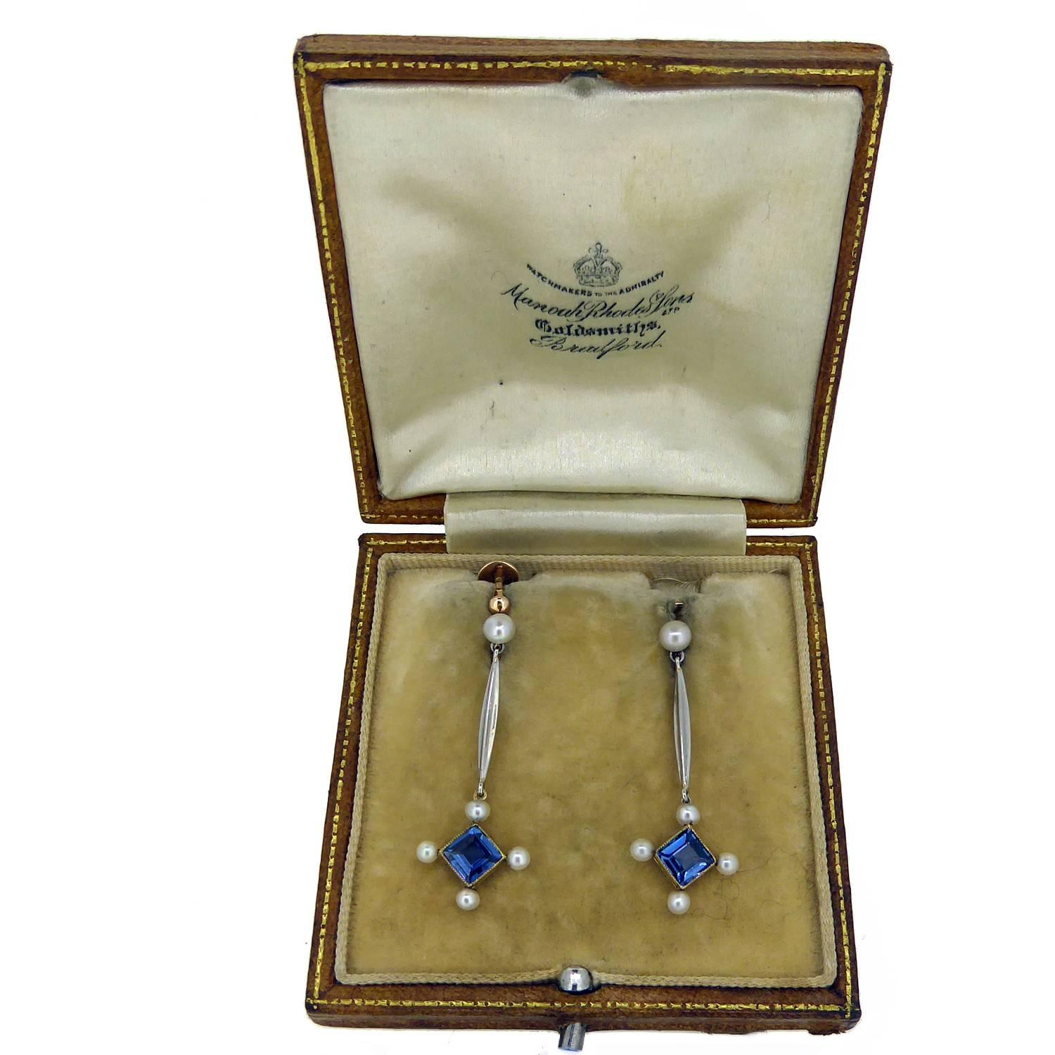 Beautiful sapphire and seed pearl earrings from the Edwardian era.  In a drop style, the earrings feature a square cut sapphire of slightly violet blue colour in a square rub over setting with a millegrain edge.  The sapphires are enhanced by the