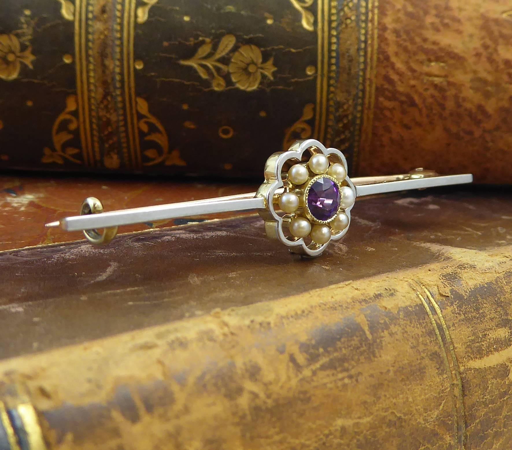 A very pretty Edwardian brooch featuring a round amethyst of good, rich colour with a pearl border all set in an open floral wire work surround.  The bar is a narrow, square cross section of yellow metal with a white top testing as approx 15 carat