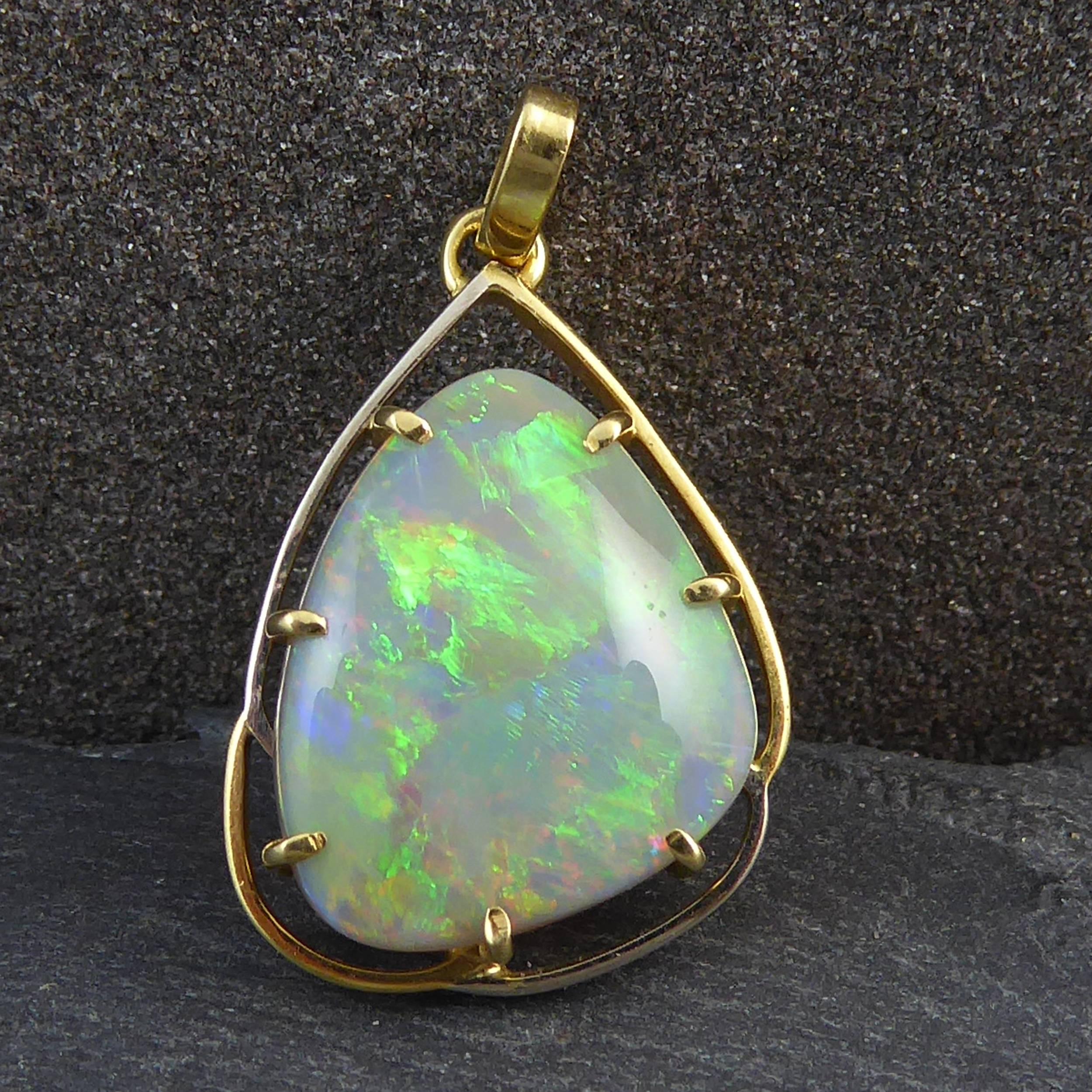 An opal set pendant comprising a spectacularly coloured opal cut in a free form, triangular cabochon shape.  The opal has a white base colour with strong green and minor orange and indigo play of colour.  Measuring approx. 0.75 x 0.56 x 0.18 inch