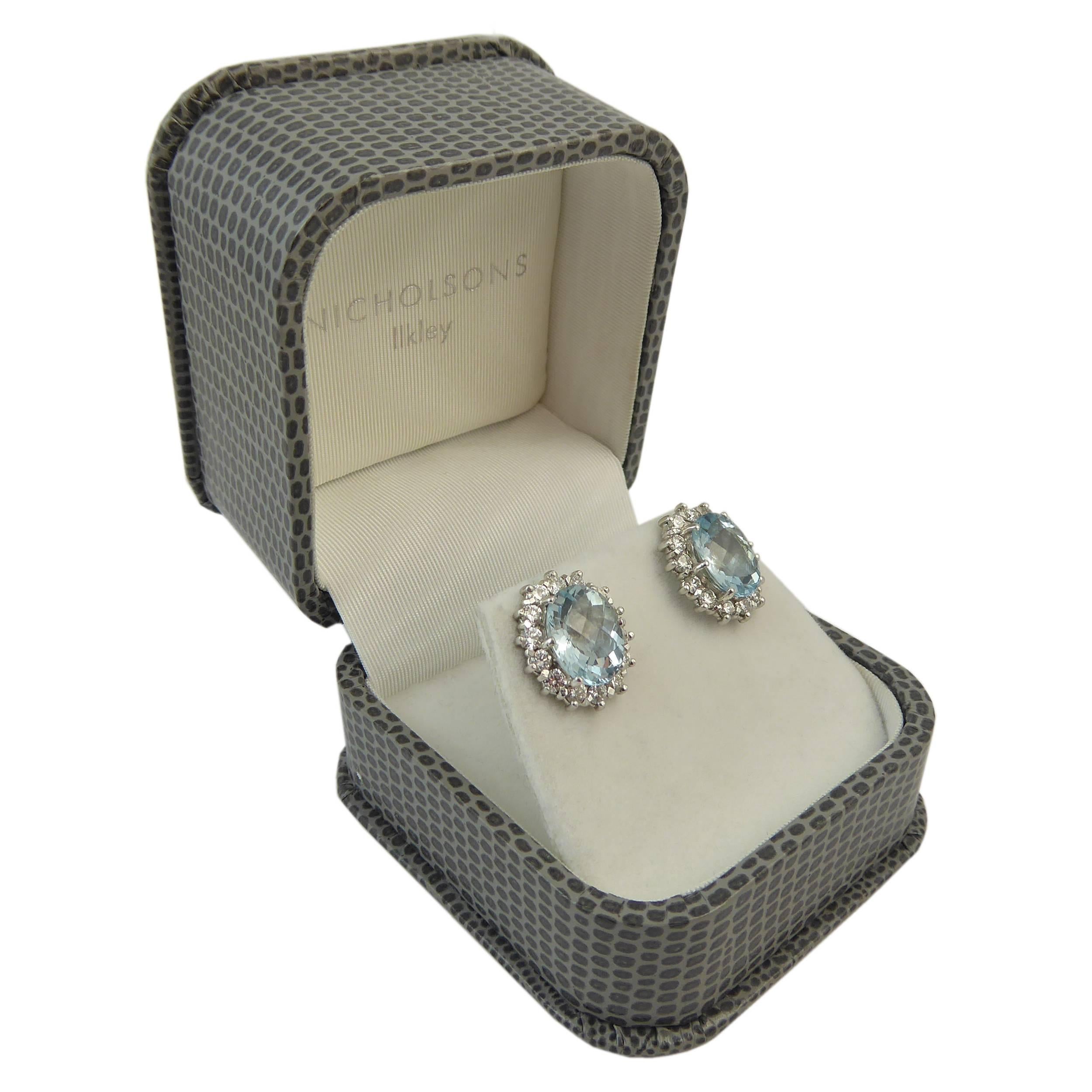 A pair of vintage earrings from the 1980s in an exquisite cluster style.  Each earring features an oval mixed cut, pale to medium blue aquamarine to a surround of 14 brilliant cut diamonds all claw set in 18ct white gold.  The combine carat weight