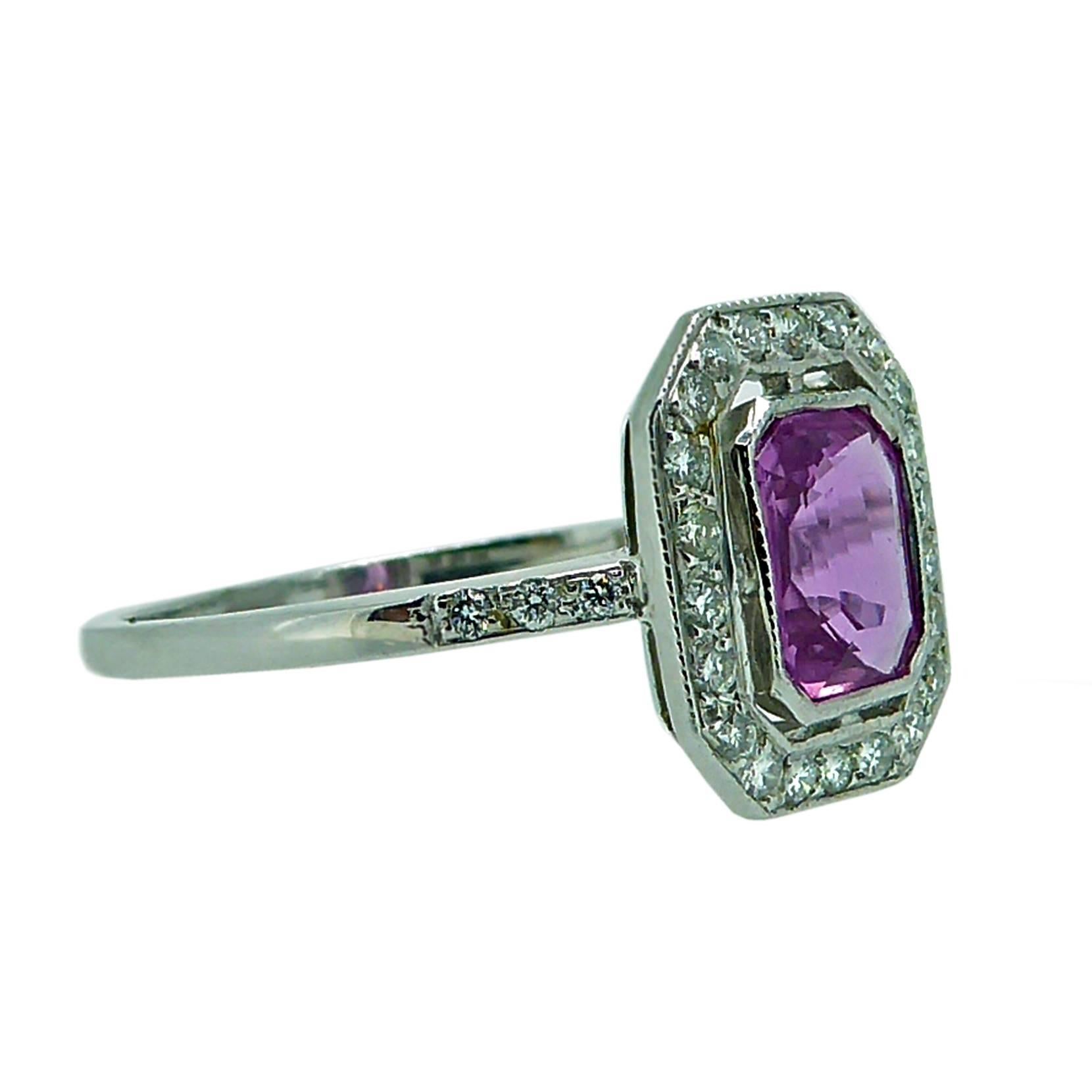 A very pretty pink sapphire of octagonal step cut is the centrepiece to this elegant and feminine cluster ring.  The sapphire sits in a white rub over setting and has a surround of 22 grain set brilliant cut diamonds to shoulders set with a futher