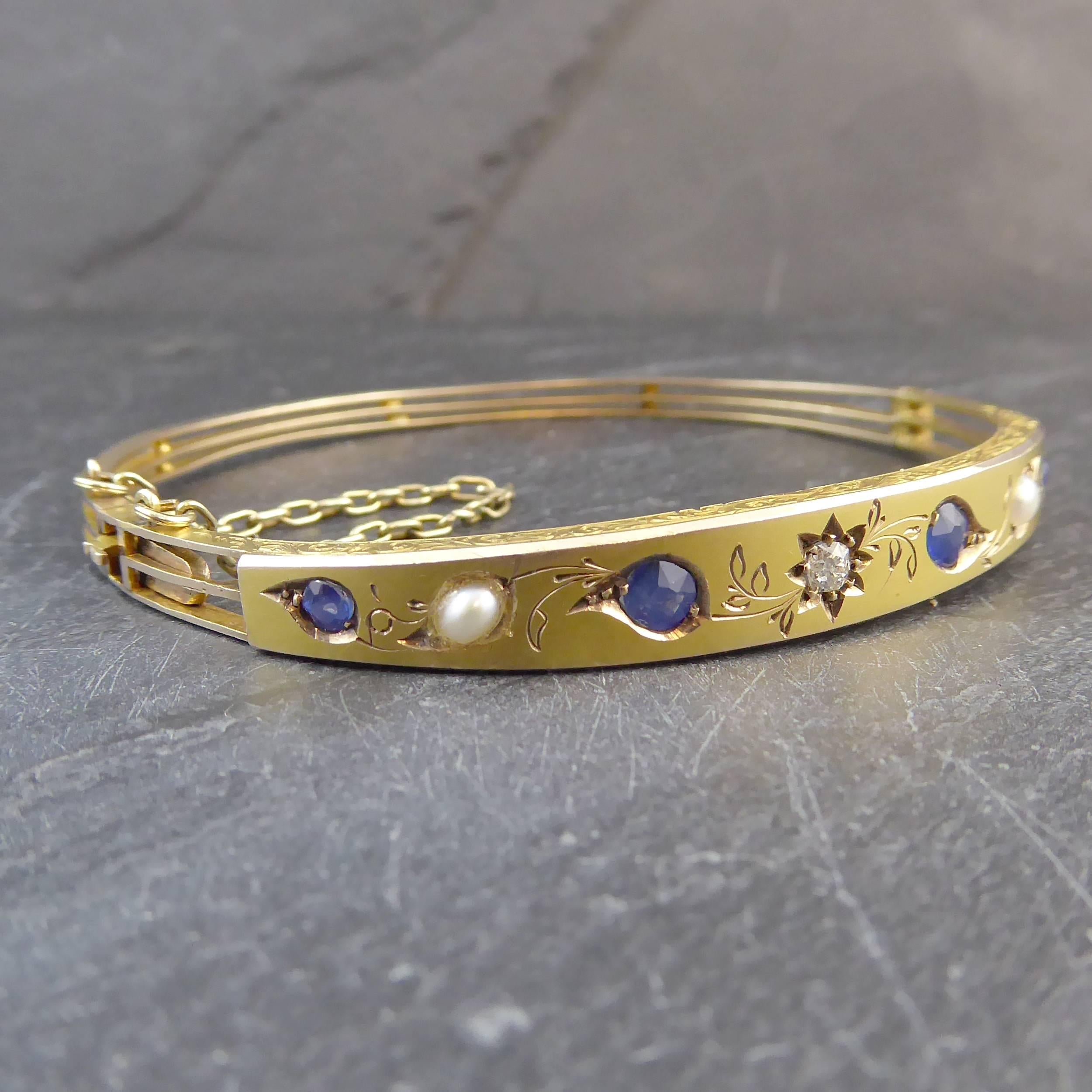 A diamond, sapphire and pearl bangle from the Victorian era, circa 1890-1900.  The front of the bangle is a curved and tapering section of satin matte finish 18ct yellow gold displaying from the centre a gypsy star set, cushion shaped, old cut