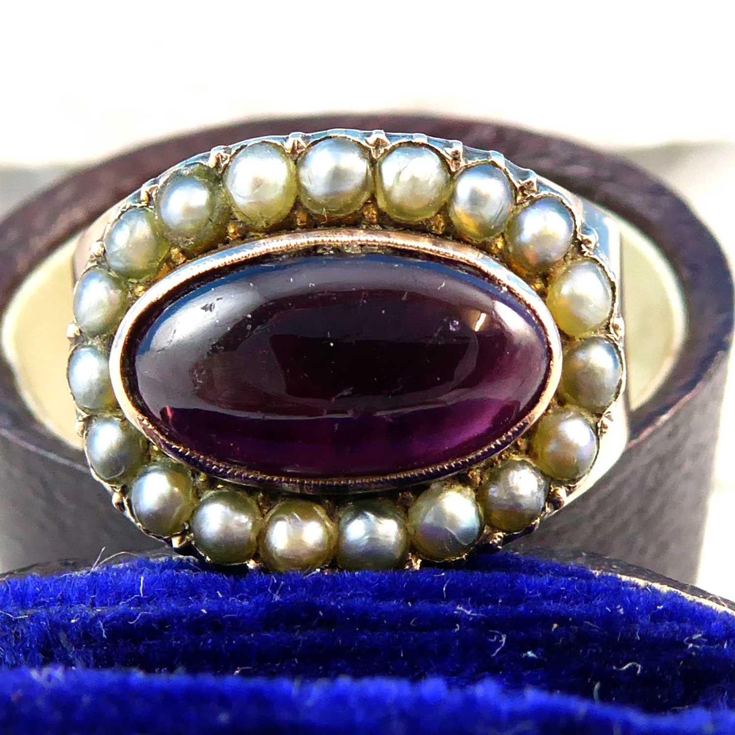 An antique garnet and pearl cluster ring in the Georgian style.  Dating from the 1850s, the ring is centrally set with a fully rub-over set, oval cabochon cut almandine garnet, measuring approx. 11.60mm x 6.10mm.  Set within a rose gold collet with