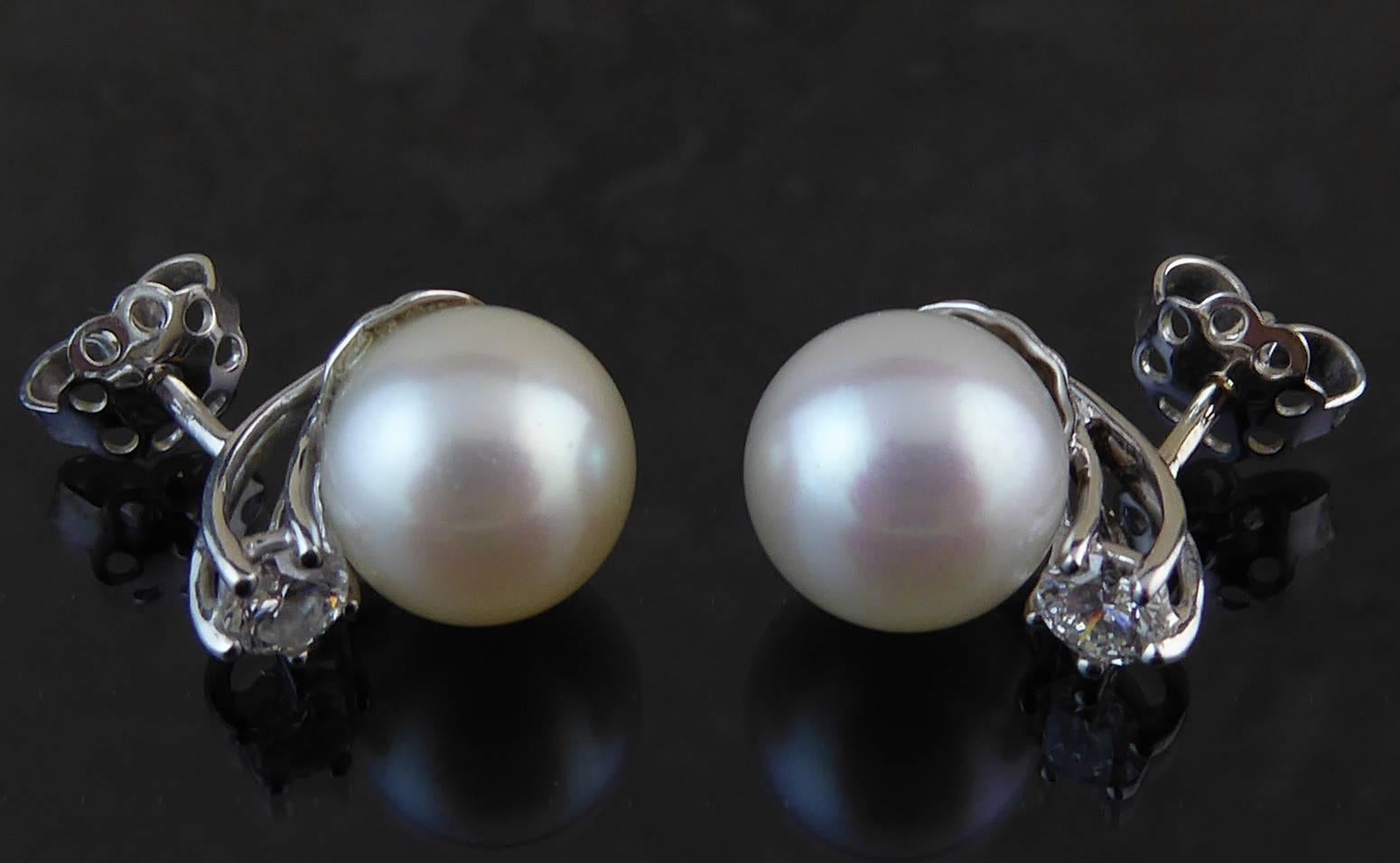 Two South Sea cultured pearls approx. 9.7mm wide of light creamy rose colour and medium lustre.  The pearls are set on white gold cup mounts with four elongated curved bars terminating in a brilliant cut diamond, each diamond being approx. 0.23ct