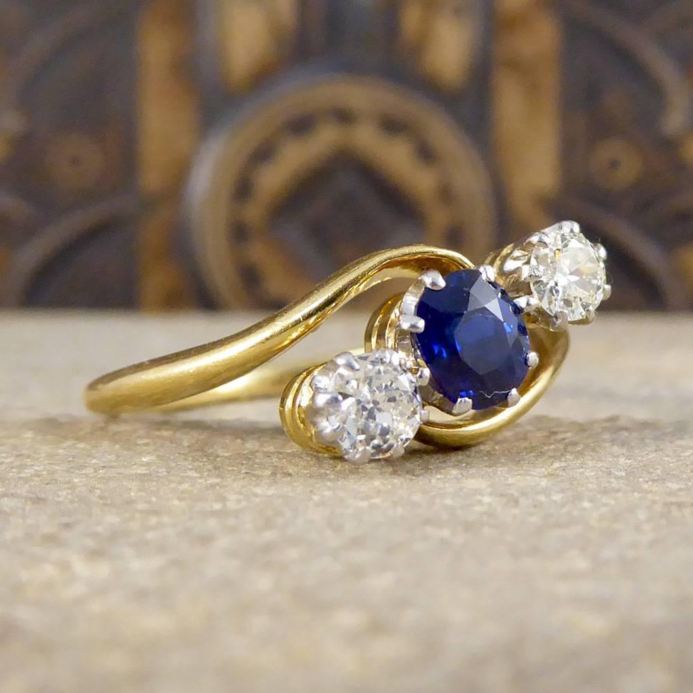 This beautiful Sapphire and Diamond three stone twist ring has been hand crafted in the Edwardian Era. The twist design mount displays a feature 0.50ct vibrant blue Sapphire with two clear and bright Diamonds sat at either side, mounted in a 18ct