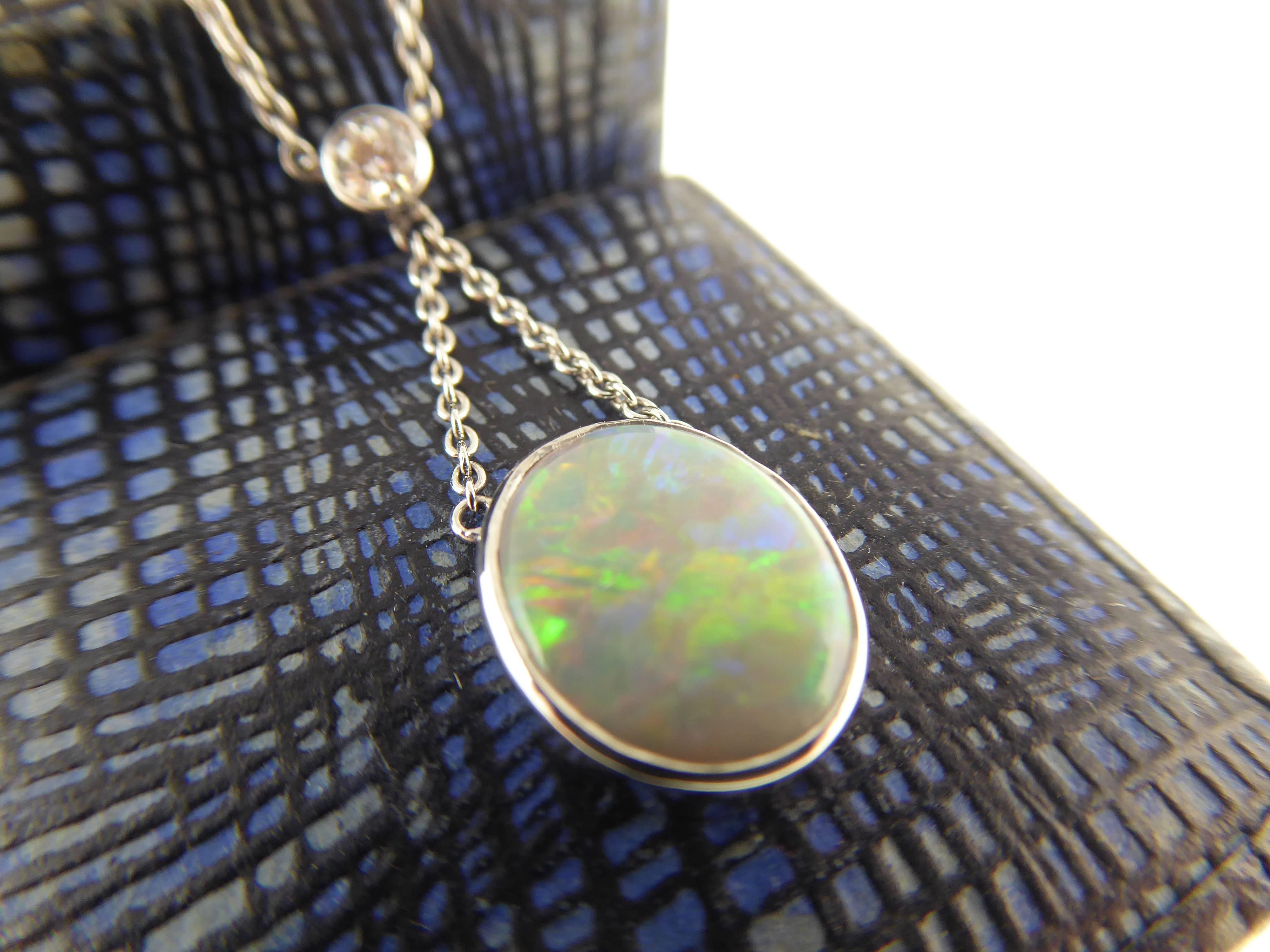 An elegant and refined Edwardian style opal and diamond pendant.  The oval cabochon cut opal displays a beautiful play of red/blue/green fire and is suspended by fine white gold chain from a brilliant cut diamond in a white rub over