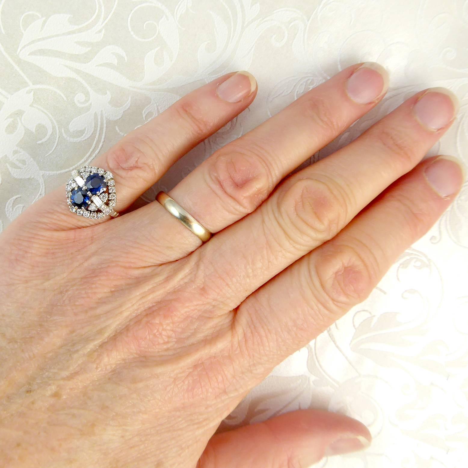 A vintage sapphire and diamond cluster ring from 1991.  Set to the centre with two round, blue sapphires placed one above the other pointing down the finger and with two brilliant cut diamonds and one baguette cut diamond to each side forming a
