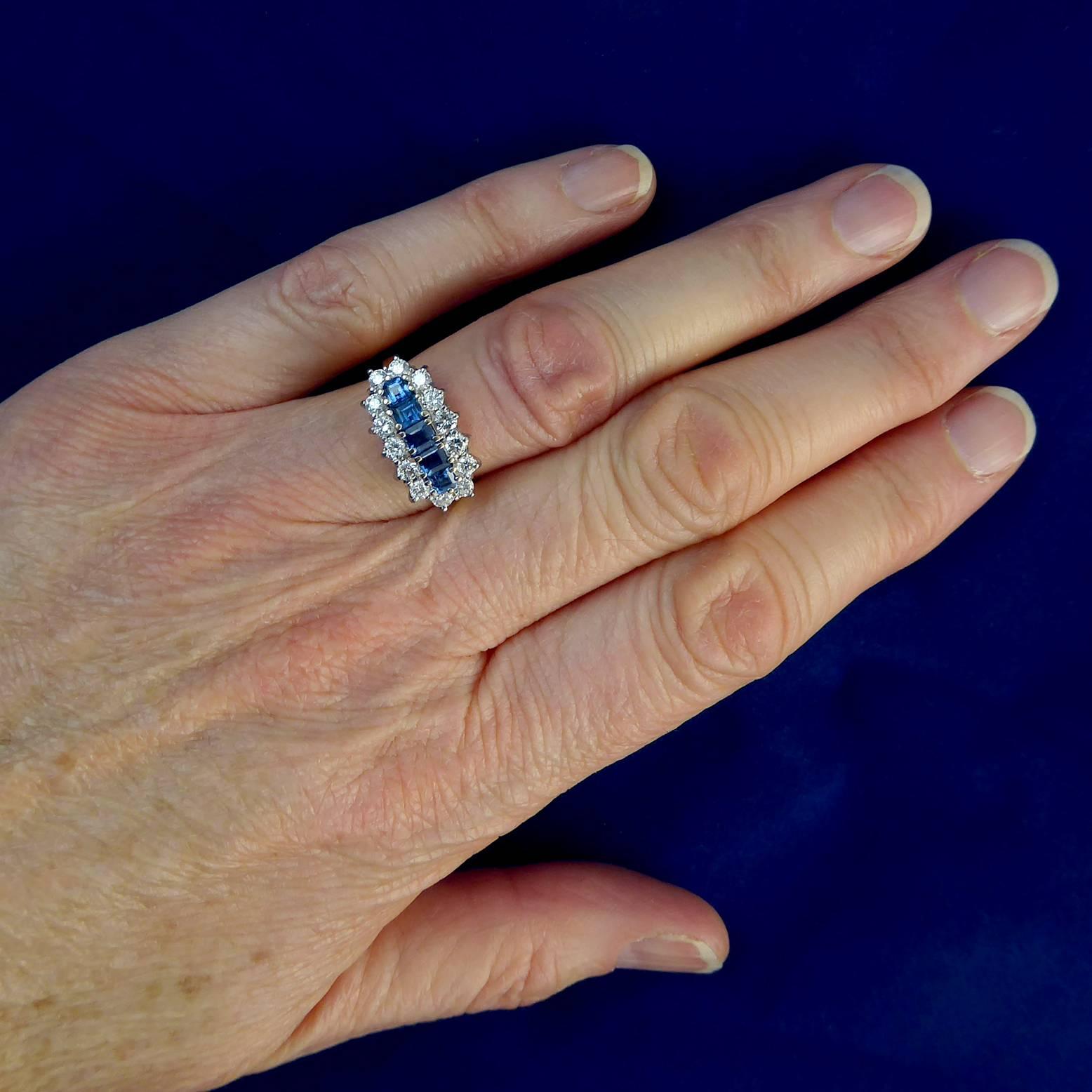 Vintage 1980's sapphite and diamond ring set with a row of five step cut sapphires of good blue colour in a row across the finger.  The sapphires are displayed within a border of brilliant cut diamonds with all stones set in white claws to an open