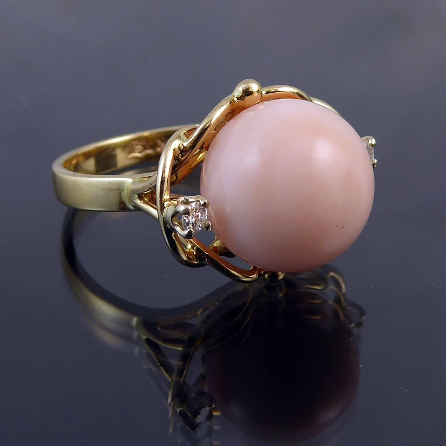 Vintage cocktail ring comprising a beautifully coloured coral of pale peach tones.  The coral is set in a simple and elegant yellow gold open work mount with gold bead decoration and a tiny sparkle of diamond to each side.  The band is a flat cross