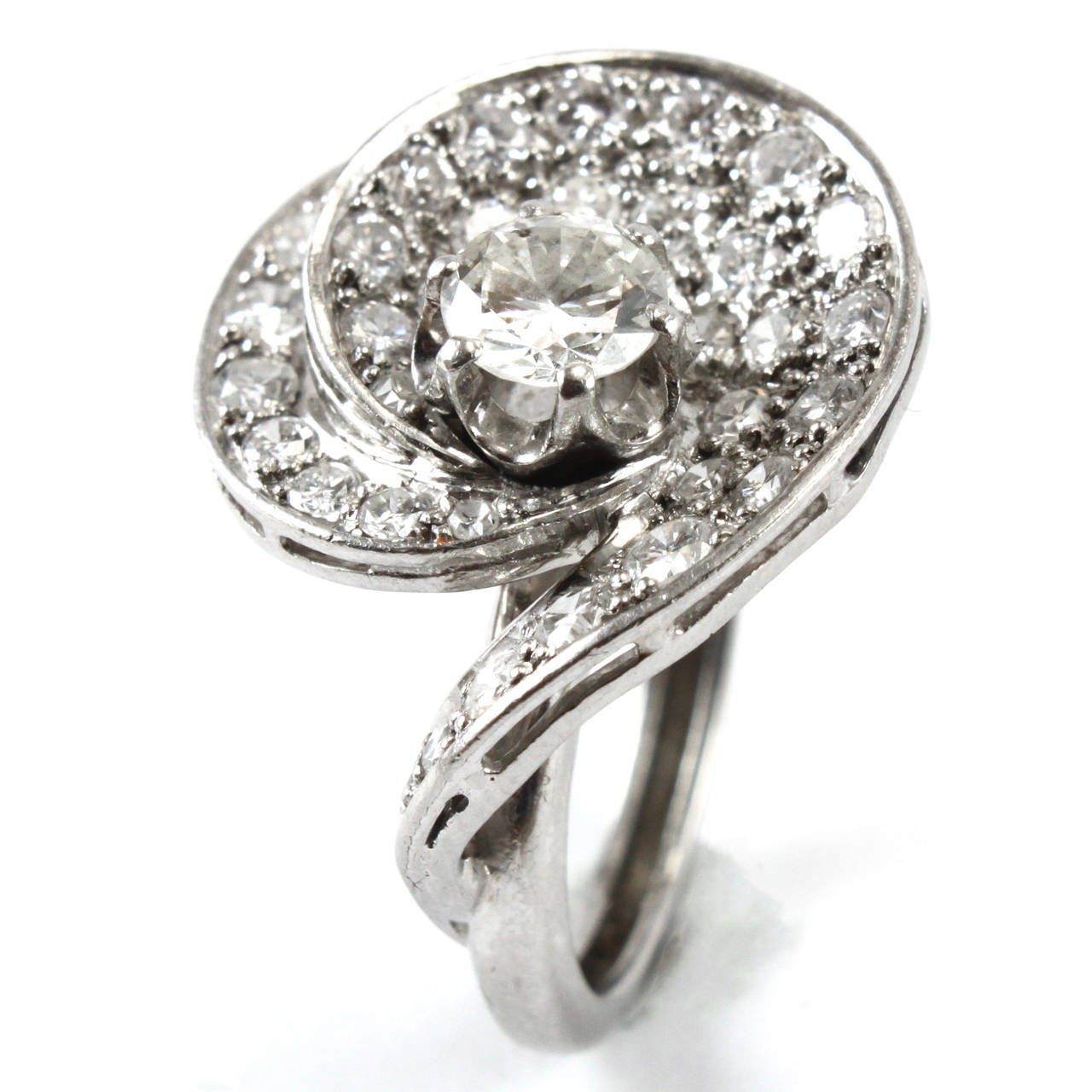 A pretty cocktail ring with a central diamond solitaire surrounded by smaller brilliant cut diamonds in a swirl design. The central diamond weighs circa 0.75ct and is of G/H color and SI1 clarity. The smaller diamonds weigh circa 2 carats in