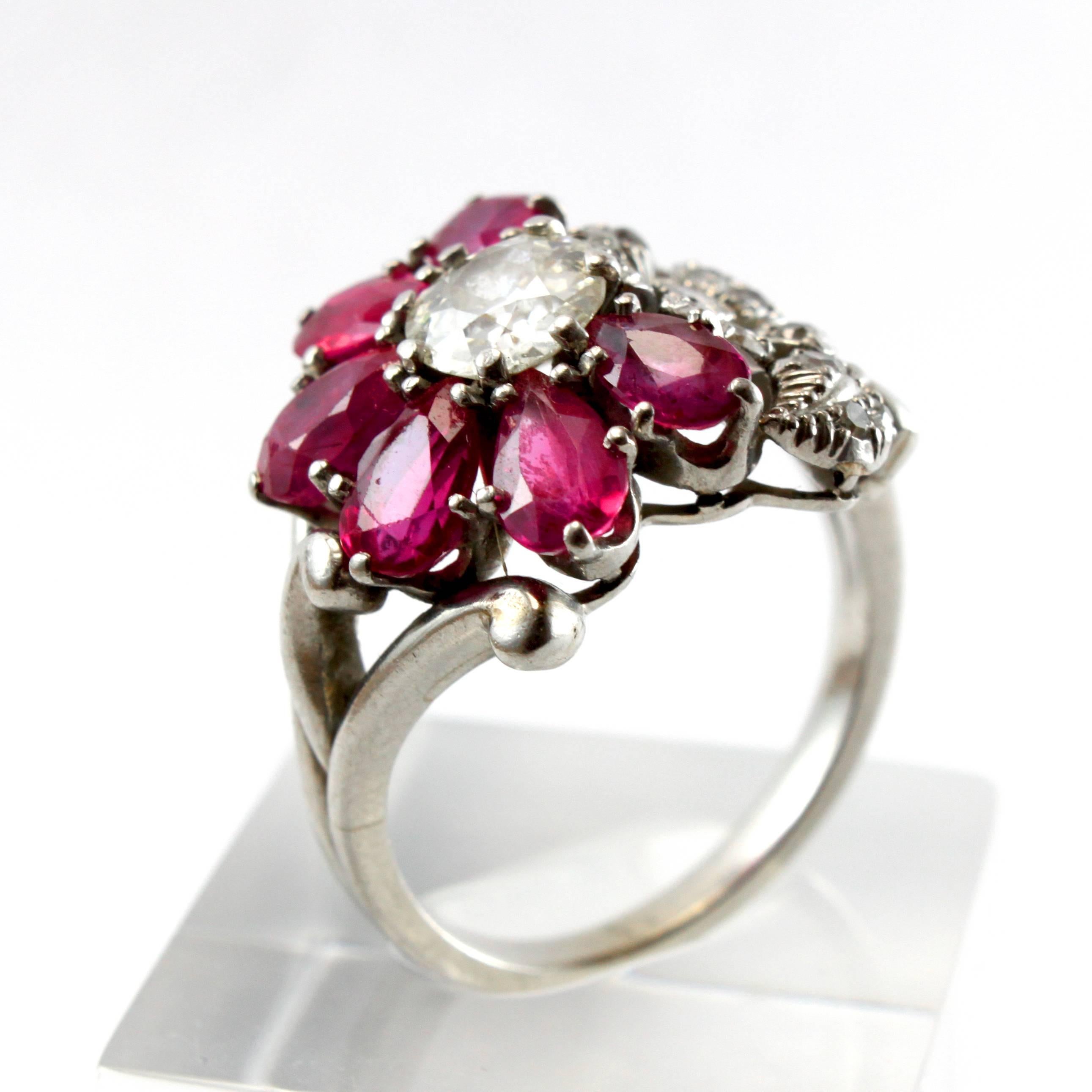 An unusual Ruby and Diamond Cluster Ring, ca. 1940s.

Centring an old-cut diamond of ca. 0.85ct (ca. I/VS1), surrounded by six ruby petals, accentuated by another flower studded with diamonds.

Ring size 8 (can be altered).