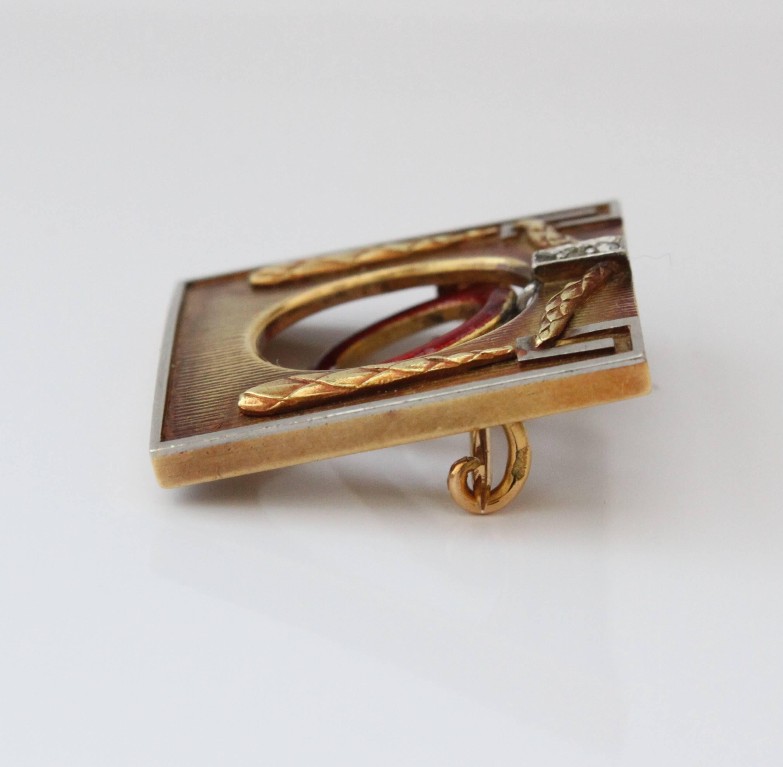 A brooch by Theodor Fahrner from the Jugendstil period depicting an arc with swinging elements. The brooch is in 18k yellow gold and has red enamel, a natural pearl and diamonds in the middle painting the picture of the swinging element. It is