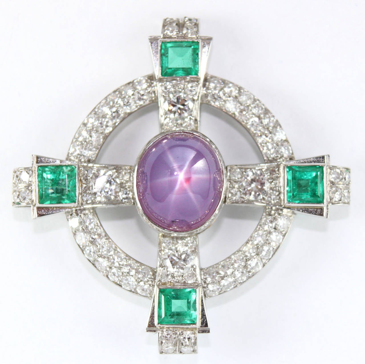 A beautiful Celtic Cross brooch in platinum with a rare purple star sapphire in the centre that is accentuated by diamonds and 4 square cut emeralds. 

The sapphire has a perfect 6-ray star in the middle of the stone (it is a very strong and sharp
