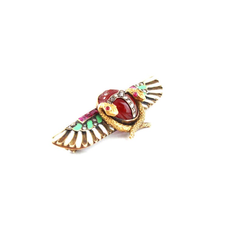 A fine Egyptian Revival Brooch by Carl Bacher from circa 1880s, depicting in the center a carved scarab with inlaid diamonds, and the back carved with an Egyptian motif. The scarab is surrounded by two snakes with ruby eyes and enamelled wings set