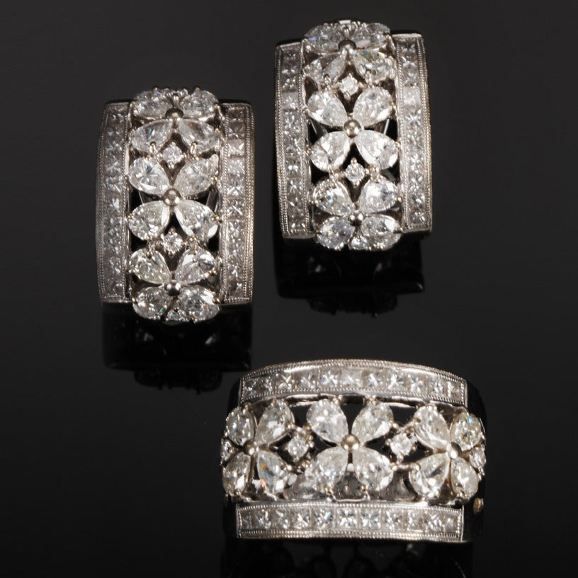 A matching diamond ring and earrings set with a floral motif set in 18k white gold. The petals are set with pear-shaped diamonds and have a round brilliant cut in between them. The sides are set with princess cut diamonds. The total diamond weight