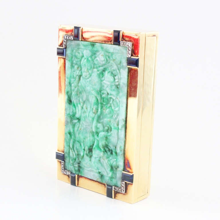 This is a unique Art Deco gold box from the 1920s depicting a Chinese woodworker in a forest, carved in green jadeite, surrounded by rectangular cut sapphires and rose cut diamonds, set in 18k yellow gold. The box opens with a patented mystery