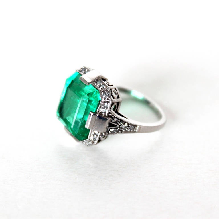 The lovely Art Deco ring in platinum is set with a big Columbian emerald, weighing 9.02ct. The shape of the emerald is very distinct as it beautifully integrates with the design lines of the Art Deco ring. The sides of the ring are set with single
