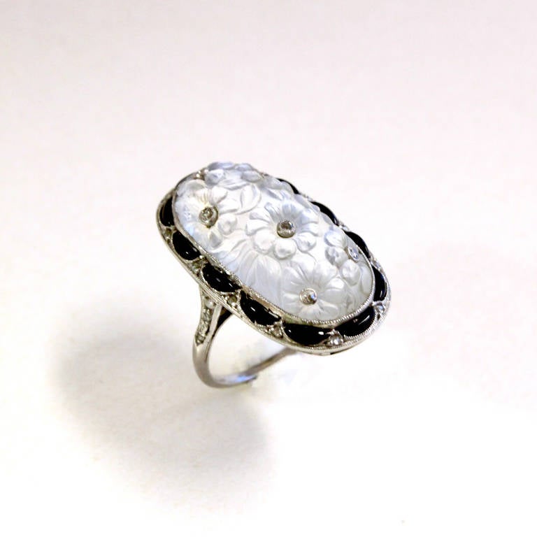 A very beautiful Belle Epoch Ring. The center stone is a big Moonstone with floral carvings that shimmer a soft blue Moonlight when worn. The carved flower centers are set with diamonds. The ring border features intricate work in combination with