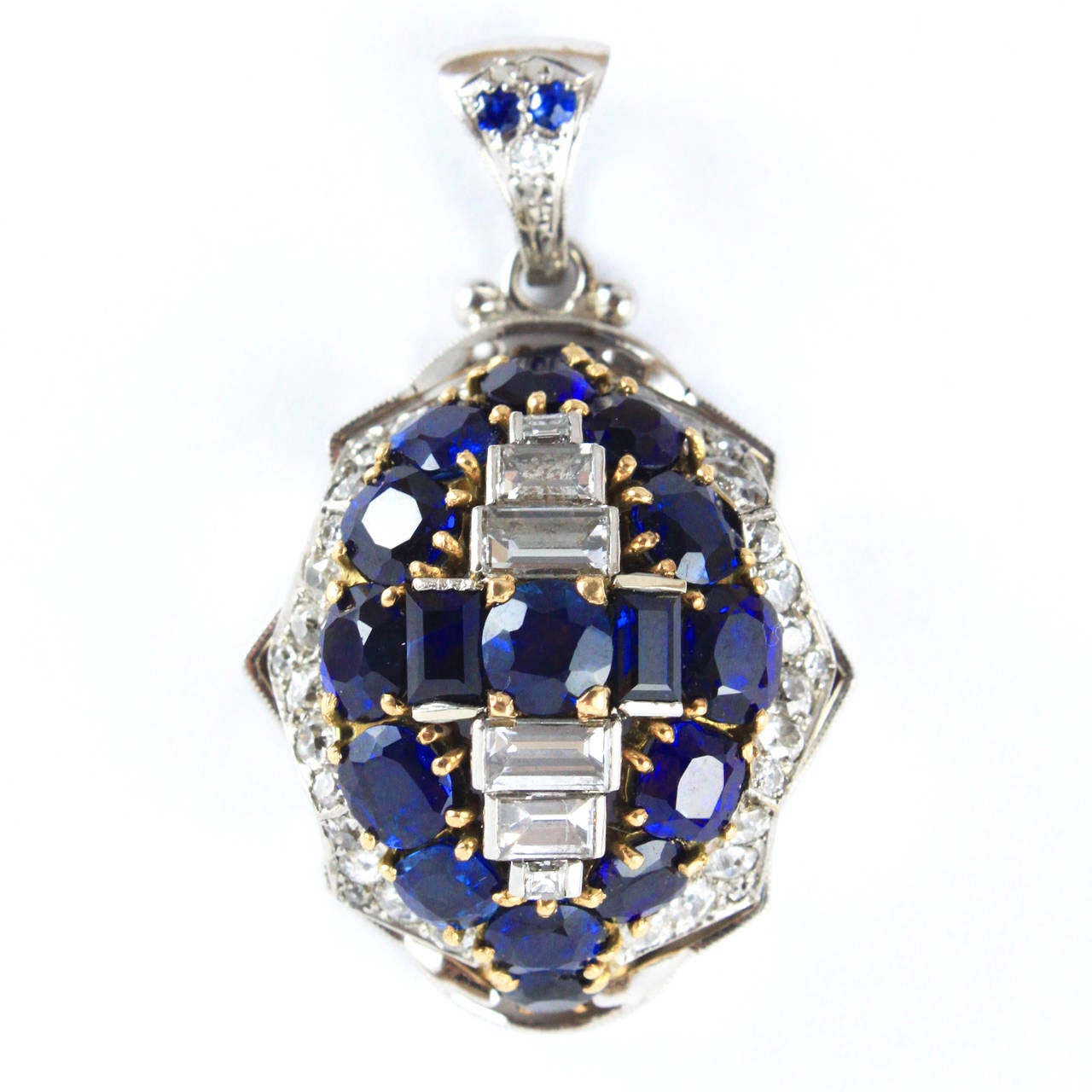 A dome shaped pendant set with diamonds and sapphires in 18k white and yellow gold. The old cut diamonds and diamond baguettes weigh ca. 2ct and the intense blue sapphires weigh ca. 7ct. The base of the pendant has intricate design carvings, it is