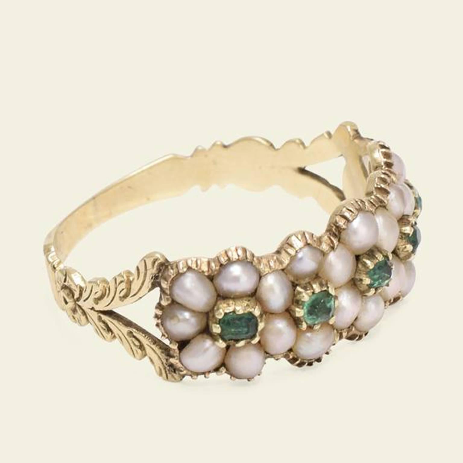 This wonderful early 19th century ring features a quintet of overlapping daisy clusters composed of seed pearls and emeralds. The stones sit withing classic Georgian crimped settings with a closed back. The ring features split shoulders adorned in