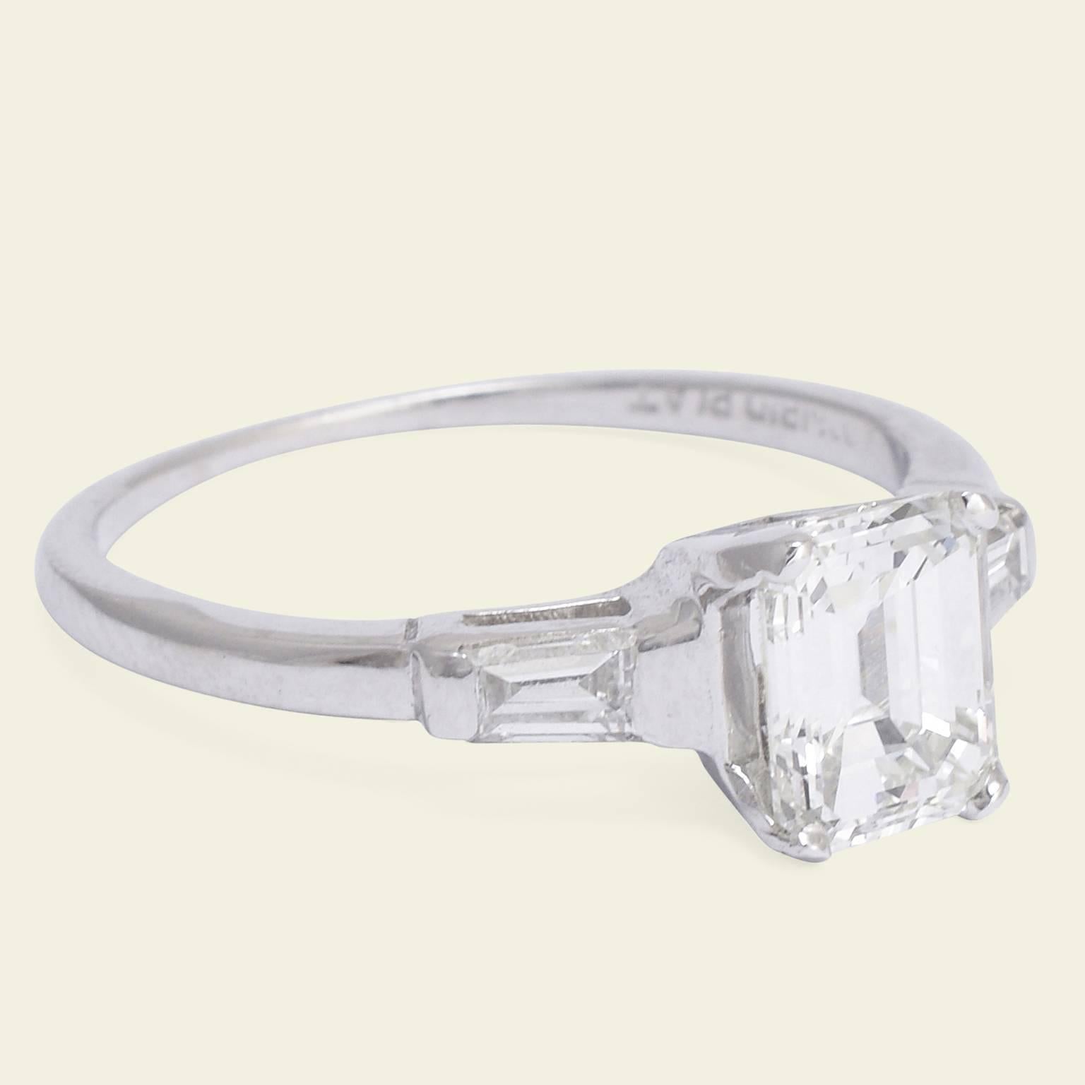 Fashioned in platinum c. 1950, this stunning engagement ring features a 1.14ct emerald cut diamond (G/VS1) accented with tapered diamond baguettes. The mounting, in true midcentury style, is very minimal with a narrow half round hoop. This ring
