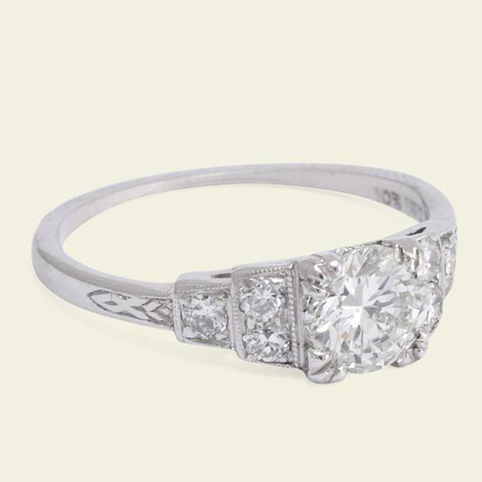 This 1920s engagement ring is made in platinum with a .72ct transitional cut diamond (F-G/VS2). The stepped shoulders are set with a total of six old European cut diamonds and feature subtle engraving where they meet the hoop. This ring comes with