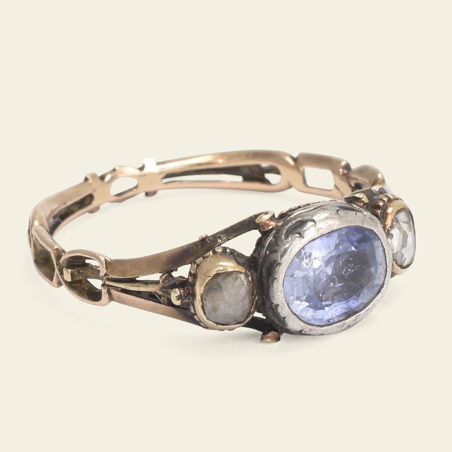 This outstanding three stone Georgian ring dates to the late 18th century. The vibrant blue oval sapphire at center is flanked by rose cut diamonds. The gemstones sit within rub over settings and the immaculate mounting features tripartite