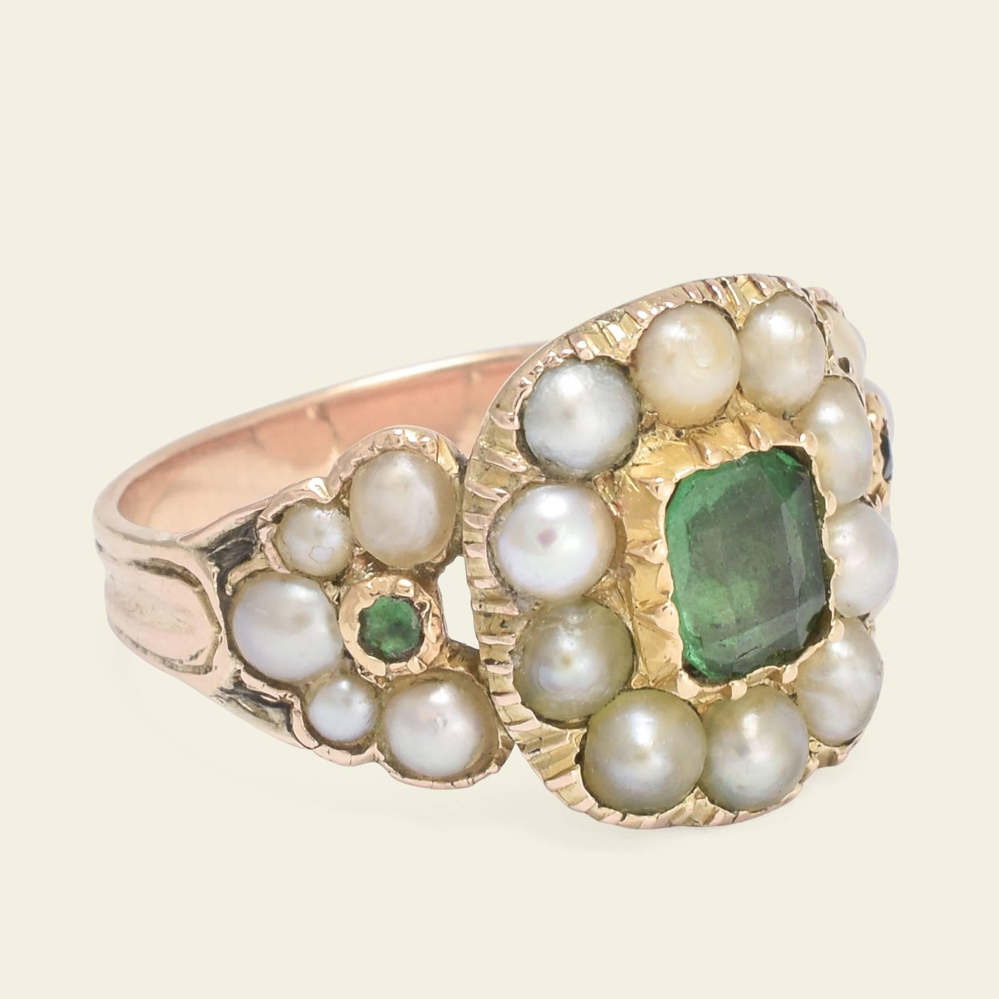 This luscious Georgian emerald and pearl ring is fashioned in 10k gold. The cluster of the head is formed by a verdant 5.1 x 5.6mm emerald haloed with pearls of subtly different hues. The demi-cluster shoulders each feature an arc of pearls