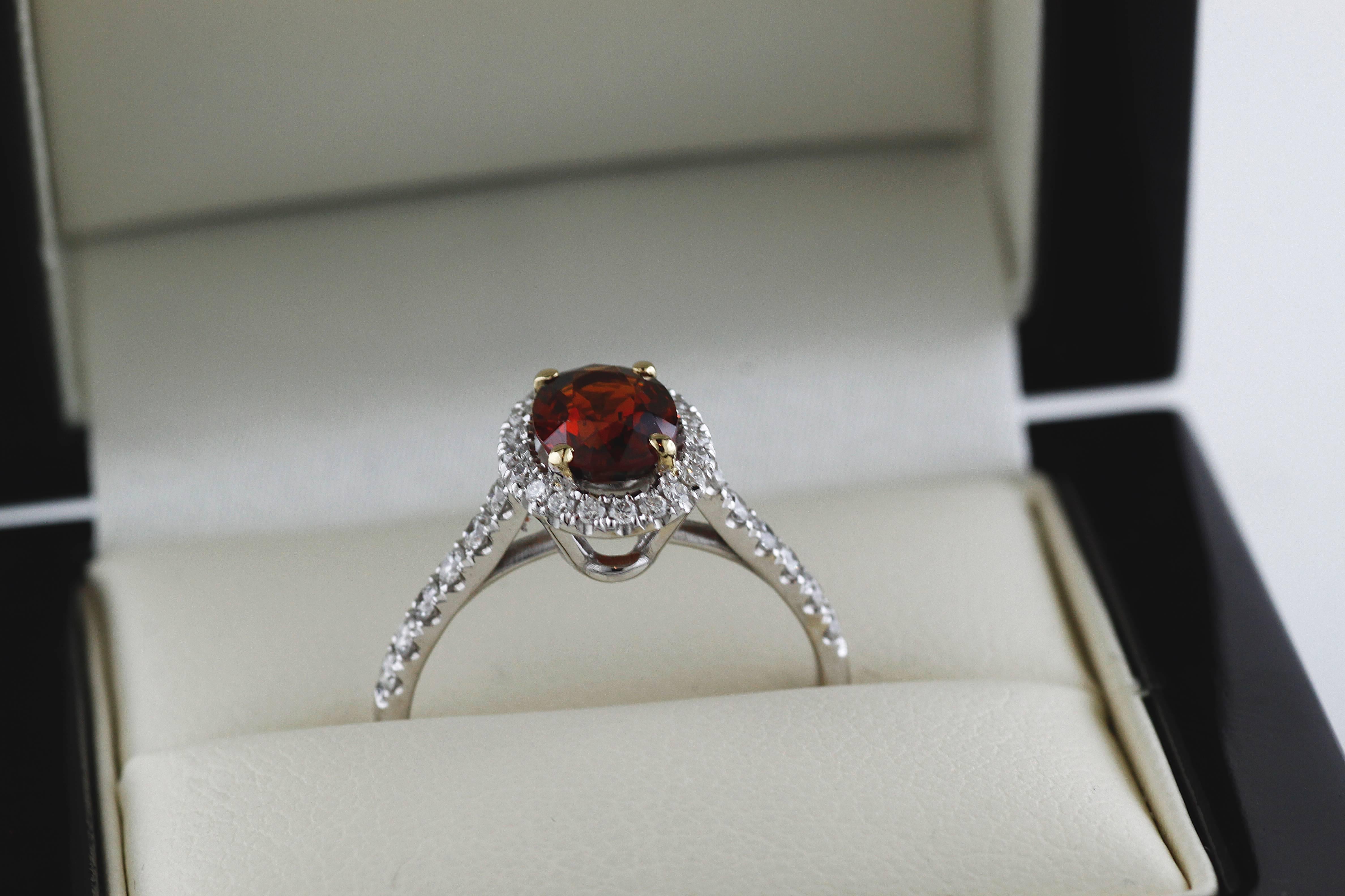 A beautiful hand-made new jewelry piece set in 18 karat white gold with an rare 1.30 carat orange transparent spessartite garnet center stone set in 18 karat yellow gold. The center stone is encircled by a row of prong-set natural diamonds with a
