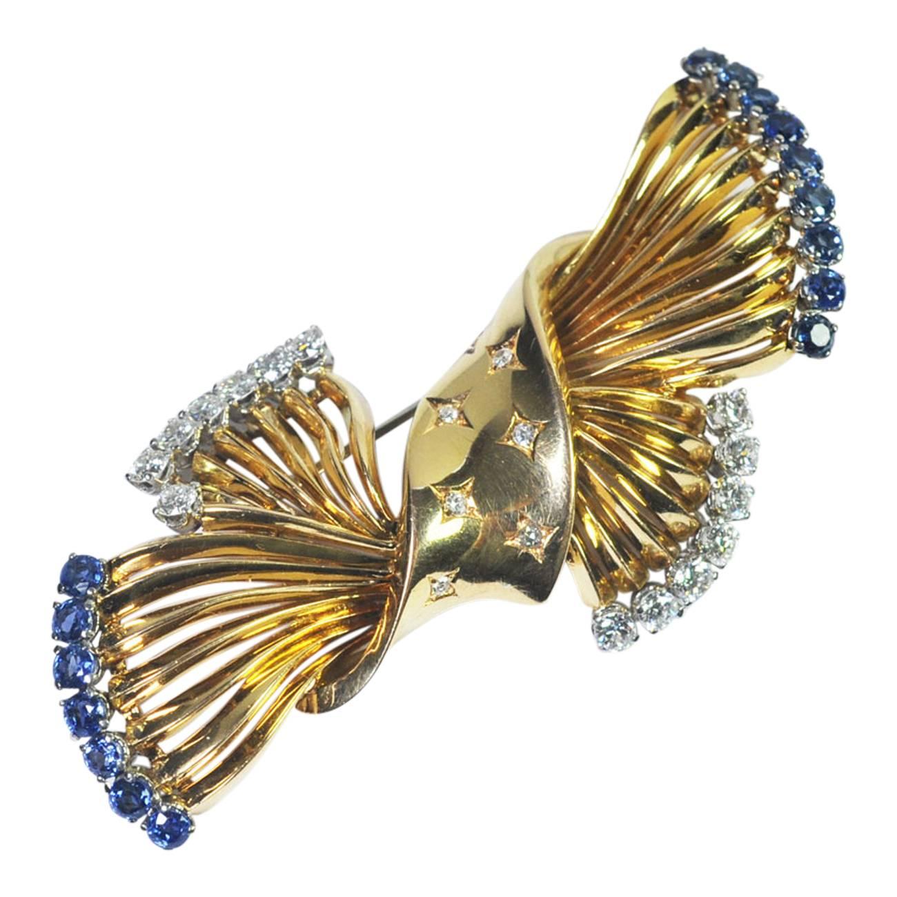 Stylish 18ct gold sapphire and diamond brooch from the exclusive Swiss jewellers, Gubelin.  Exquisitely made by master craftsmen and representing flowers loosely tied with a diamond set ribbon.  The mid blue sapphires weigh 1.56cts and the diamonds,