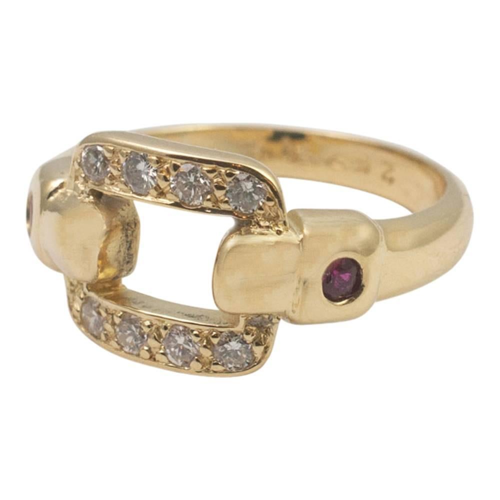 Cartier gold ring in the form of a diamond buckle with two rubies set into the shoulders.  The brilliant cut diamonds weigh 0.24ct and the buckle measures 1.2cm wide x 0.90cm deep.  Signed Cartier and numbered  Tested as 18ct gold.  Finger size M