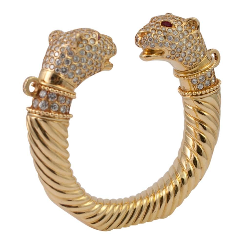 Double headed gold panther torc set with diamonds and rubies;  this dramatic bangle has two panther heads fitted with tension clips which tip back to enable the wearer to put it on; they then tip forward again to secure it in place.  Each head has